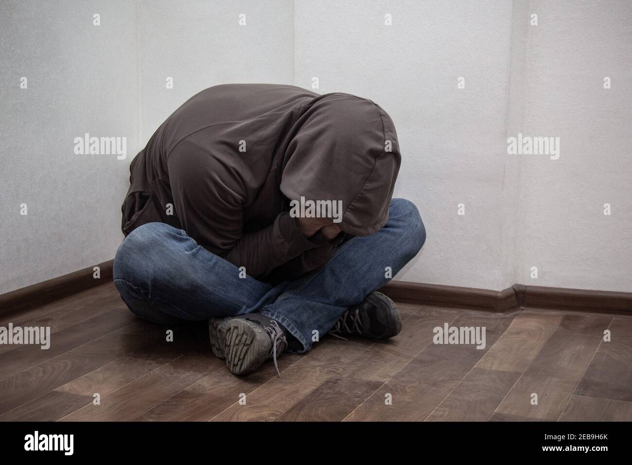 desperate young drug addict wearing hood and sitting alone in corner. concept of sadness, depressed and life problems Stock Photo