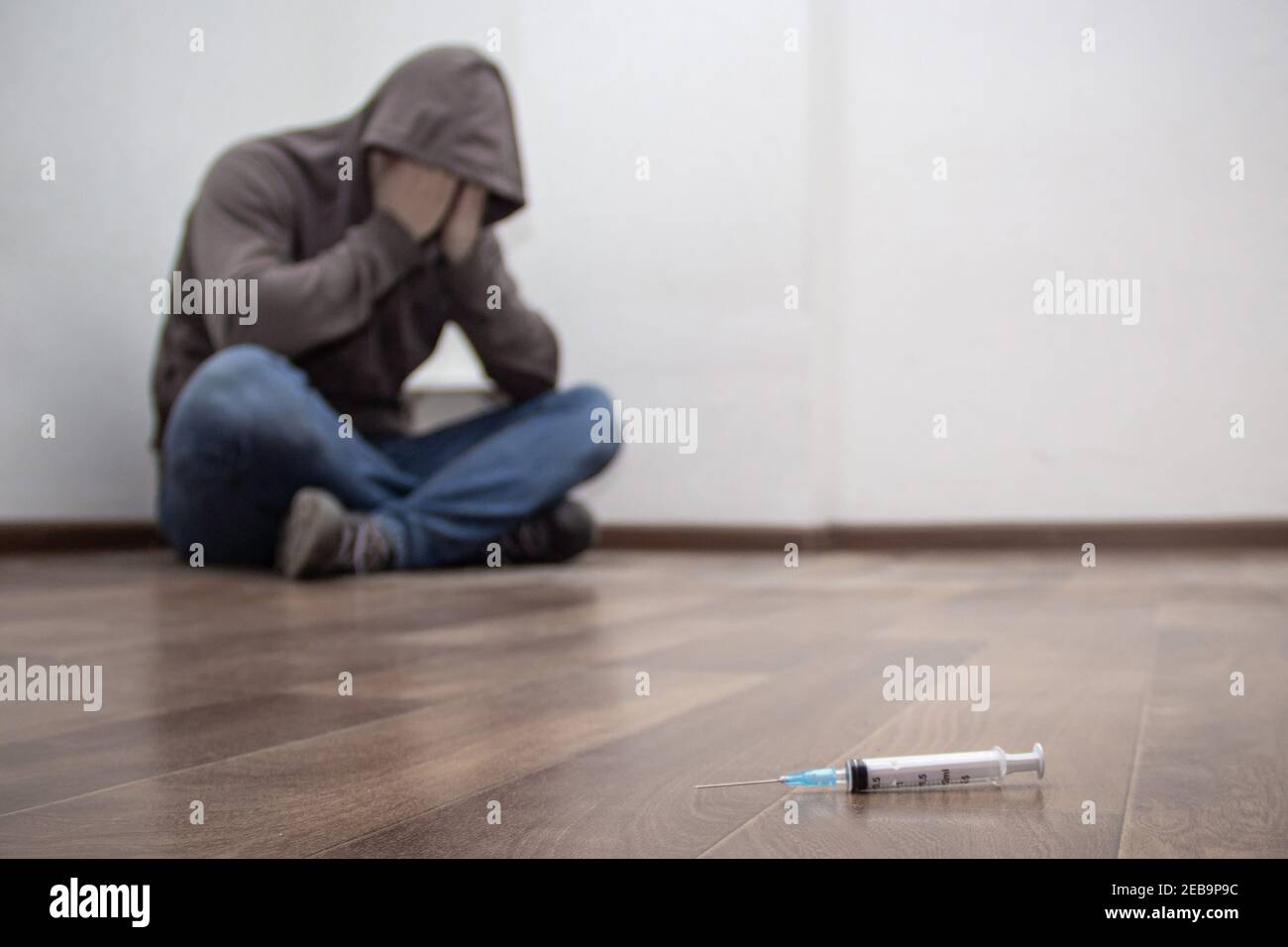 Syringe and man drug addict without of focus sitting in corner in the background. With copy space Stock Photo