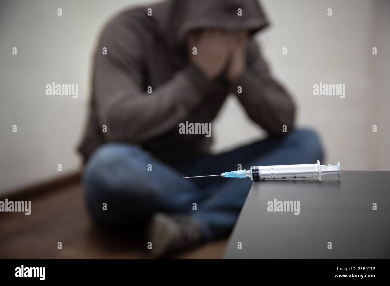 Syringe and man drug addict without of focus sitting in corner in the background. With copy space Stock Photo