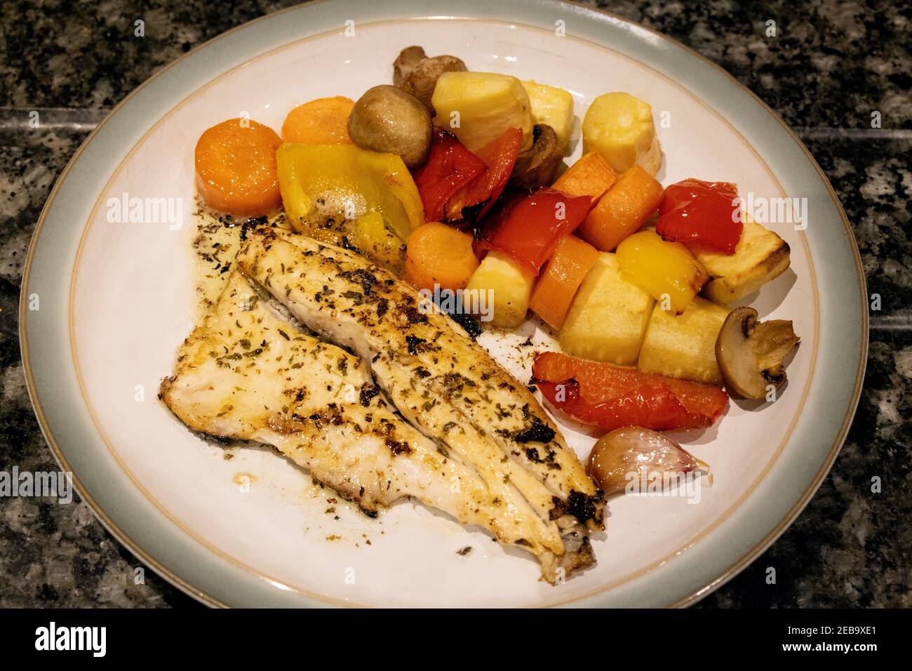Sea Bass cooked with roasted vegetables on a plate, healthy diet; Sea Bass meal with roast peppers, carrots, parsnips, mushrooms and garlic; UK Stock Photo