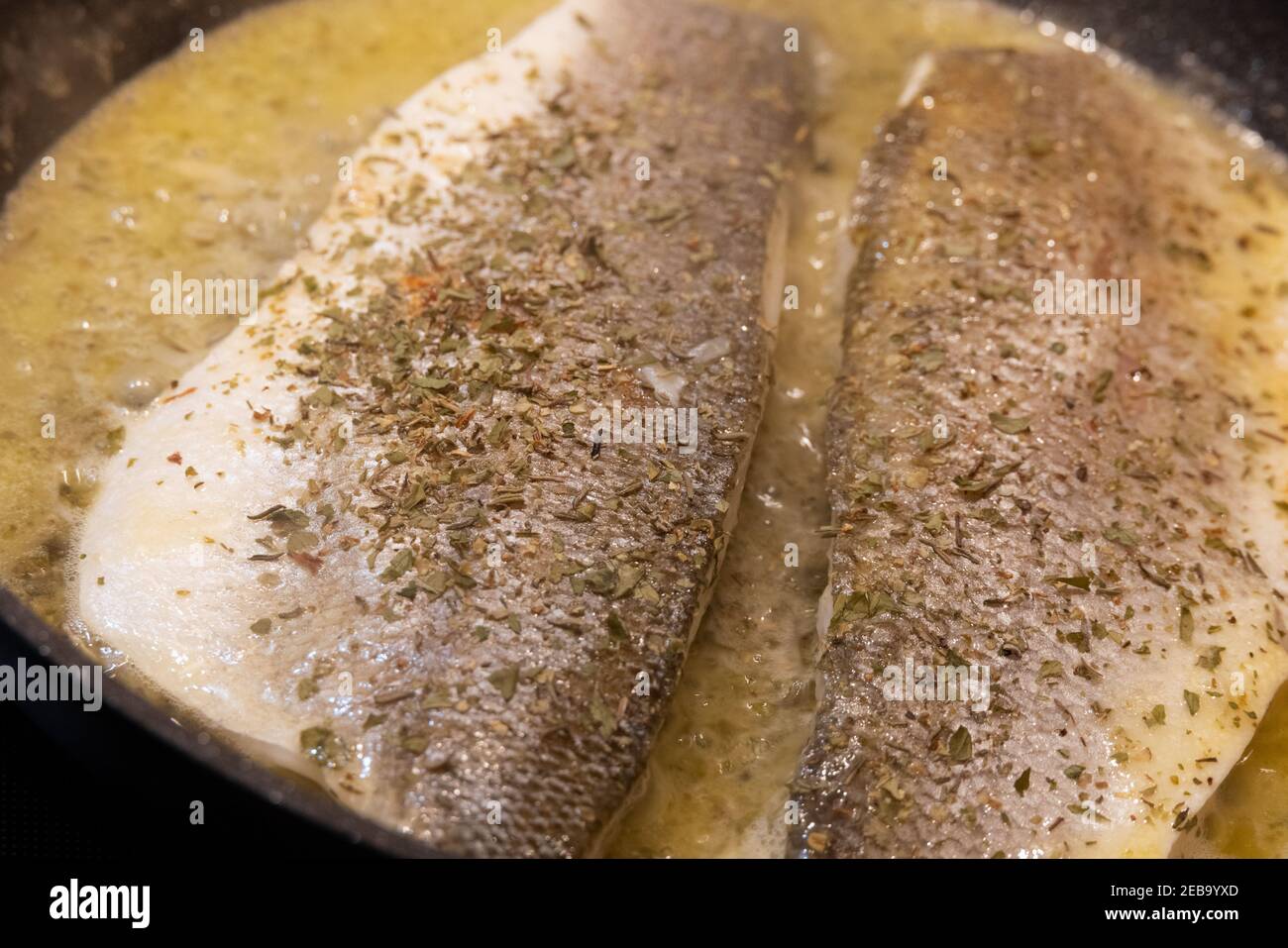 Two Sea Bass fillets cooking in butter and lemon juice with thyme in a