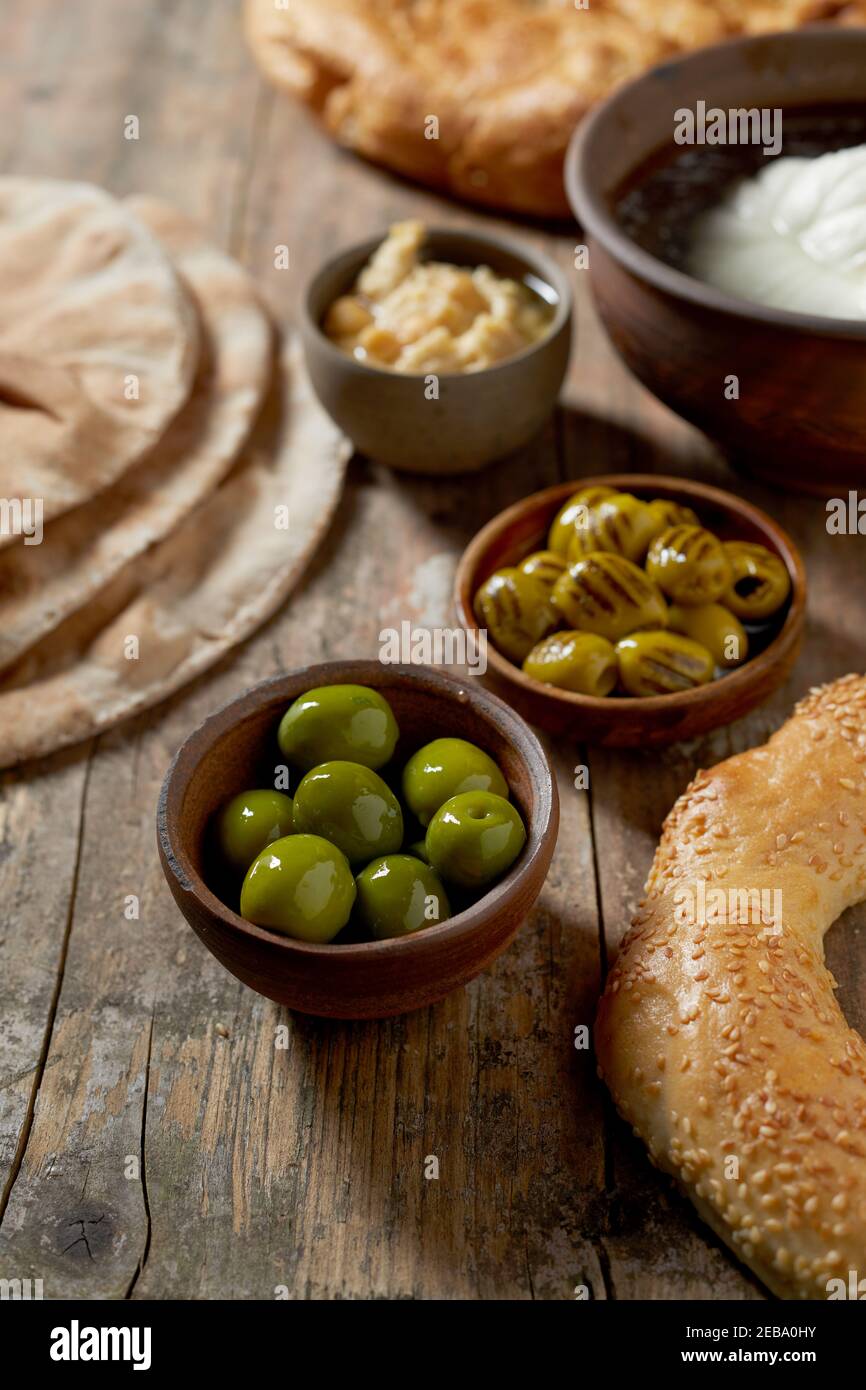Tasty breakfast with green olives, fresh mozzarella cheese in brine, chick pea spread, sesame bagel and flat bread in a vertical view on rustic table Stock Photo