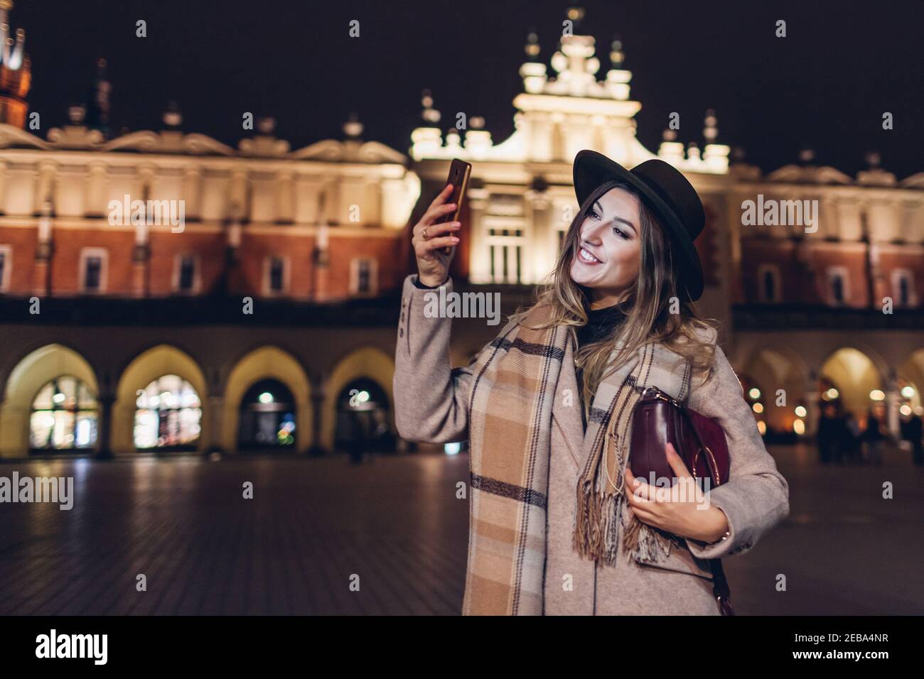 Tourist woman taking selfie on smartphone having fun at night on Market square in Krakow Poland. Travel around Europe Stock Photo