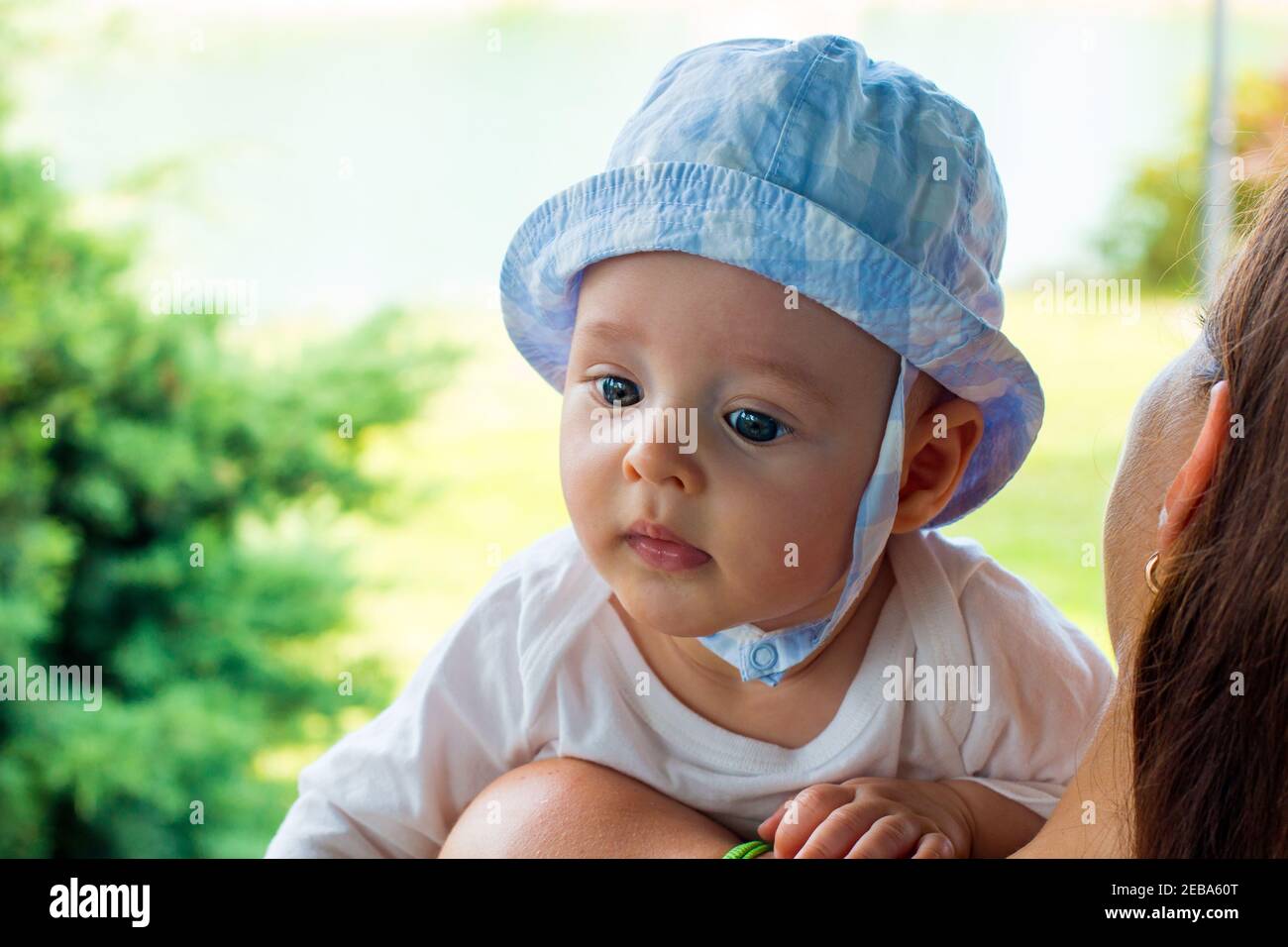 Intelligent infant face expression close up portrait, baby in cap on little head with fascinated face and focused blue eyes Stock Photo