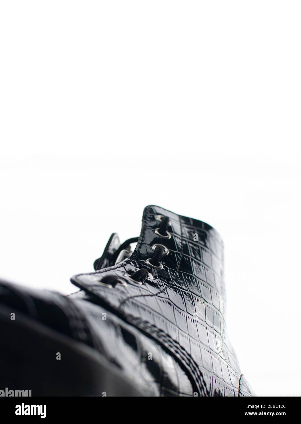 Glossy black shoe with high rubber sole and laces viewed from the front