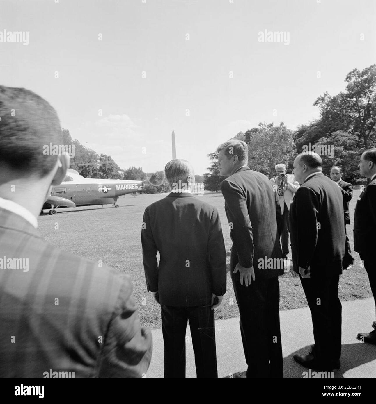 Ceremony marking Vice President Lyndon B. Johnsonu0027s (LBJ) departure on a good-will trip, 3:30PM. President John F. Kennedy watches as Vice President Lyndon B. Johnsonu2019s helicopter prepares to depart the South Lawn for his good-will trip to Lebanon, Iran, Turkey, Greece, Cyprus, and Italy. Also pictured: Ambassador of Italy, Sergio Fenoaltea; Ambassador of Nicaragua and Dean of the Diplomatic Corps, Dr. Guillermo Sevilla-Sacasa; Ambassador of Lebanon, Ibrahim Hussein el-Ahdab (al-Ahdab); National Park Service (NPS) photographer, Abbie Rowe. White House, Washington, D.C. Stock Photo