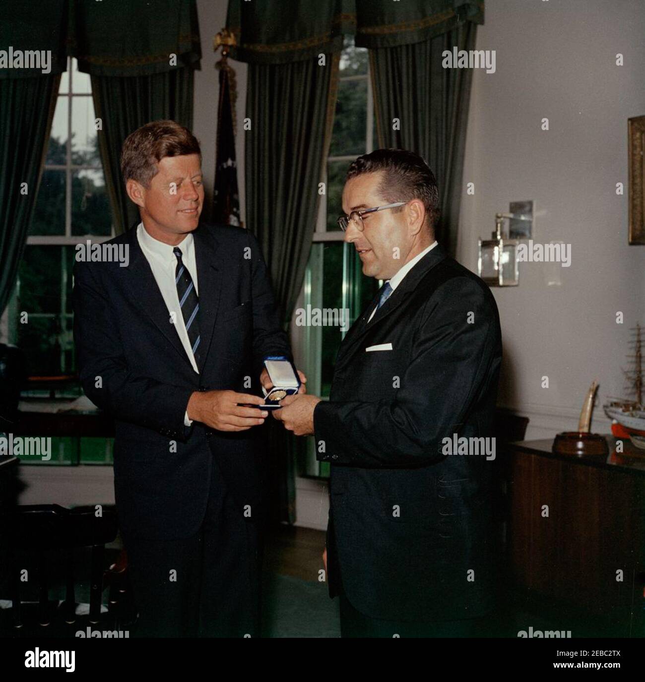 Meeting with Bernard Boutin, Administrator of General Services, 11:30AM. President John F. Kennedy meets with Administrator of the General Services Administration (GSA), Bernard L. Boutin (right); Administrator Boutin presented President Kennedy with an engraved coin commemorating the 150th anniversary of the Town of Gilford, New Hampshire. Oval Office, White House, Washington, D.C. [See also Bernard L. Boutin Personal Papers: BLBPP-MF18-003.] Stock Photo