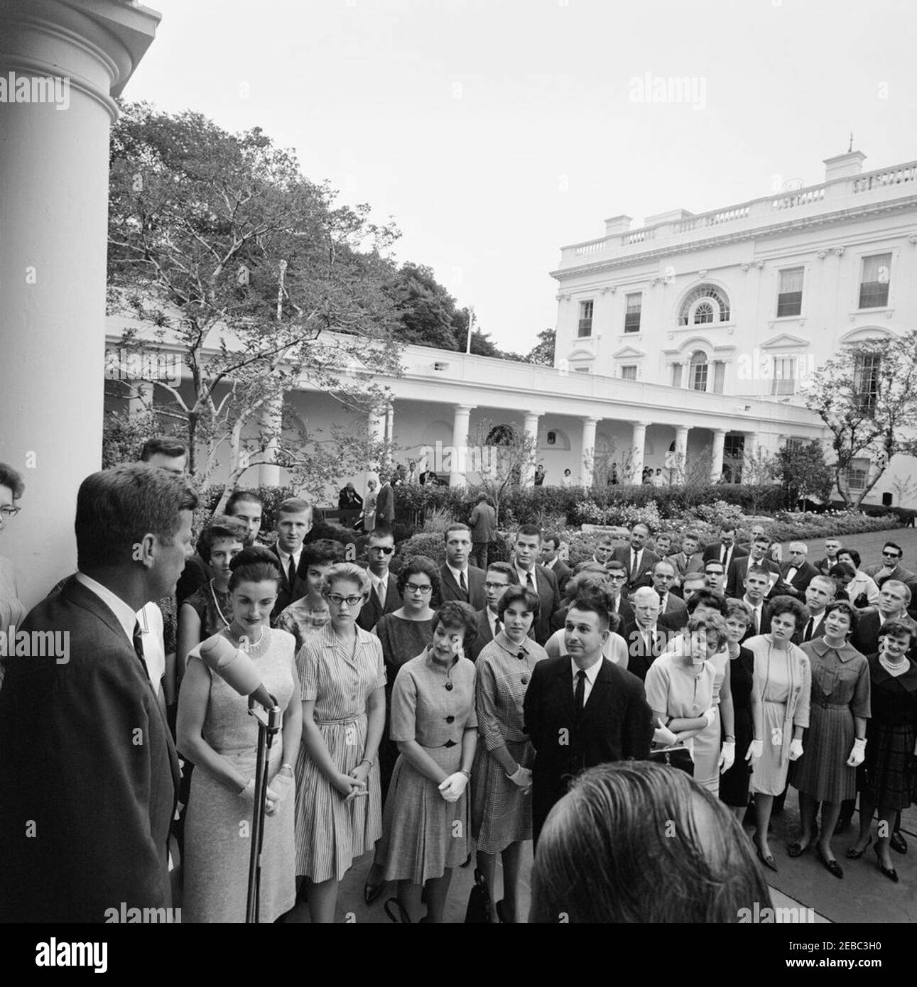 Visit of members of the Schola Cantorum, University of Arkansas, 12:15PM. President John F. Kennedy (left, at microphones) delivers remarks to members of the University of Arkansas Schola Cantorum in the Rose Garden of the White House, Washington, D.C.; founding director of the Schola Cantorum, Richard Brothers, stands at right. The choir visited the White House after winning first prize at the Guido du0027Arezzo International Polyphonic Competition in Arezzo, Italy. Stock Photo
