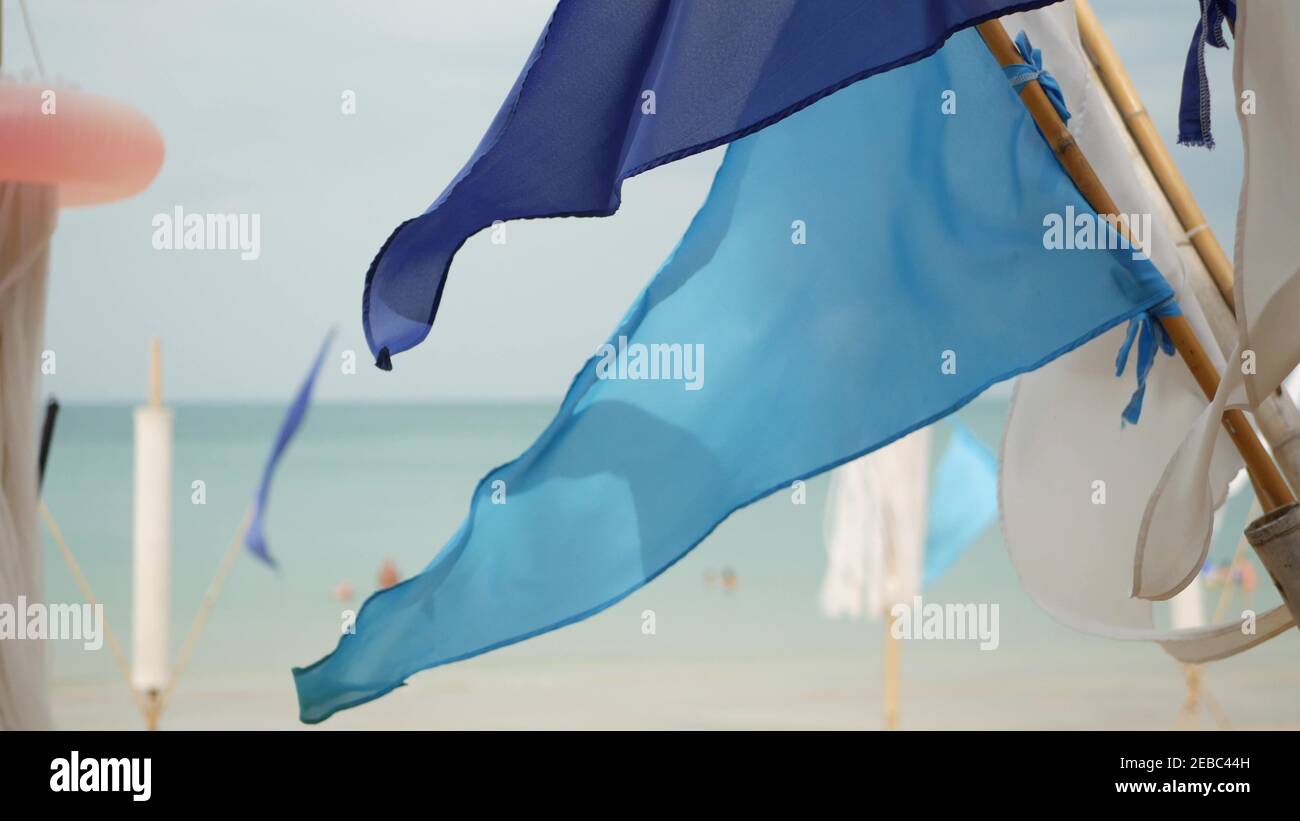 Blue flags waving in wind. Small triangular blue flags fluttering in wind in cloudy weather on tropical beach. Stock Photo