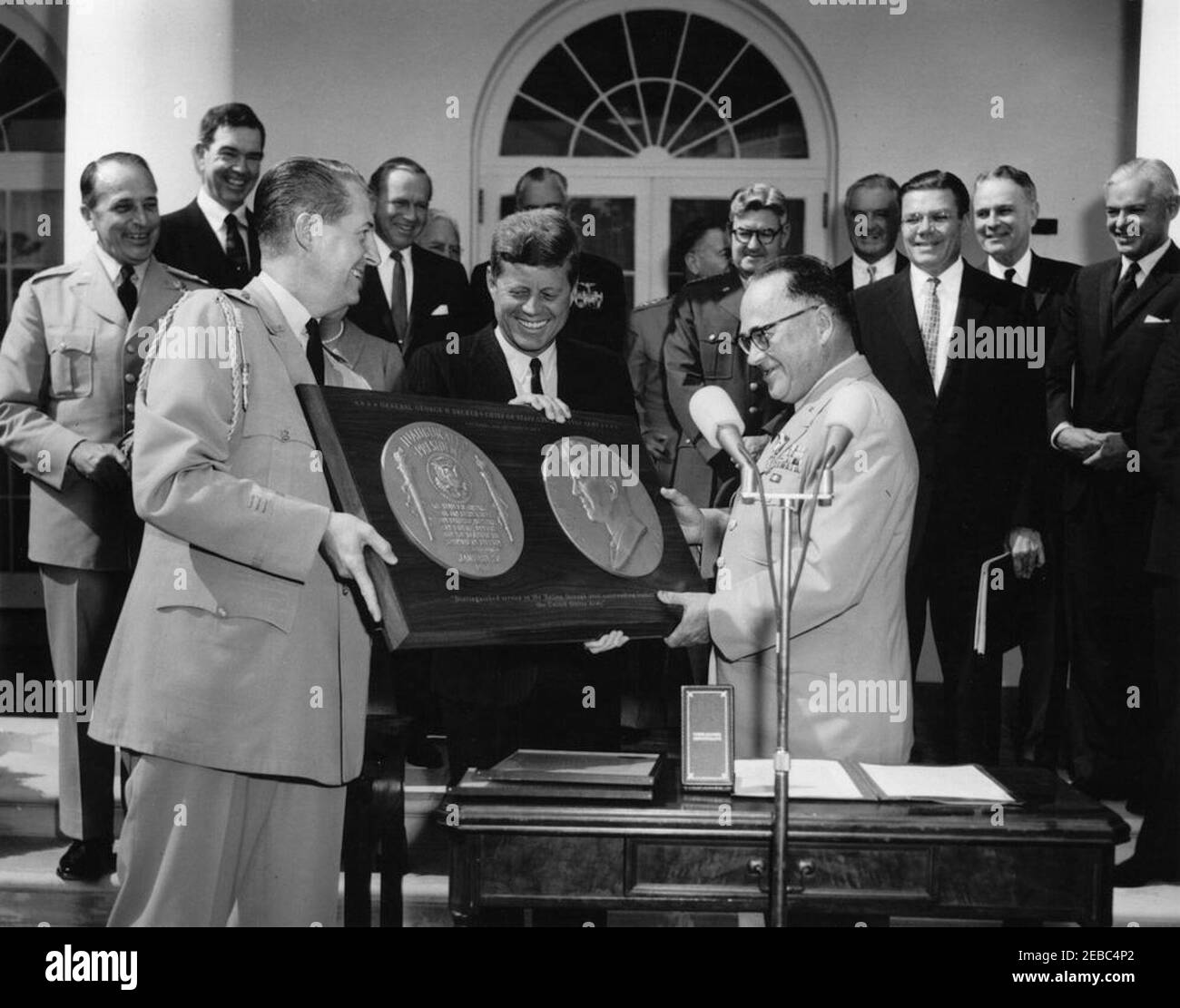 Presentation of the Distinguished Service Medal to Gen. George H. Decker, 12:05PM. President John F. Kennedy presents a gift of a plaque to retiring Chief of Staff of the United States Army, General George H. Decker (at microphones), during General Deckeru0027s Distinguished Service Medal (DSM) ceremony; Military Aide to the President, General Chester V. Clifton, holds plaque at left. Looking on (L-R): Chairman of the Joint Chiefs of Staff, General Lyman L. Lemnitzer; Representative George H. Mahon (Texas); Deputy Secretary of Defense, Roswell L. Gilpatric; Director of the Central Intelligenc Stock Photo