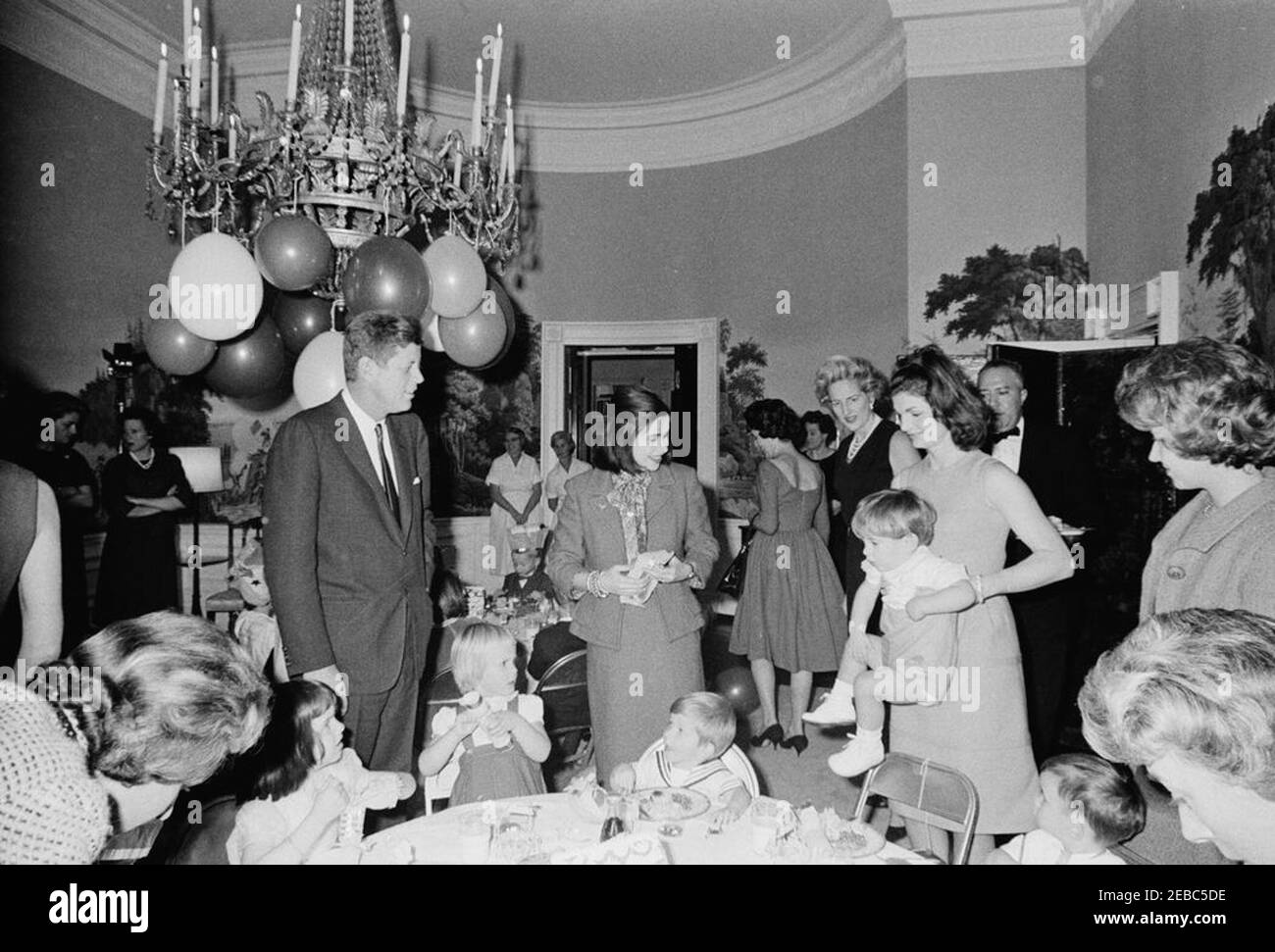 Birthday party for Caroline Kennedy and John F. Kennedy, Jr.. President John F. Kennedy and First Lady Jacqueline Kennedy attend a joint birthday party for their children, Caroline Kennedy and John F. Kennedy, Jr.; Mrs. Kennedy lifts John, Jr., at right. Also pictured: First Ladyu0027s Social Secretary, Letitia Baldrige; White House butler, John W. Ficklin. Presidentu2019s Dining Room (Residence), White House, Washington, D.C. Stock Photo
