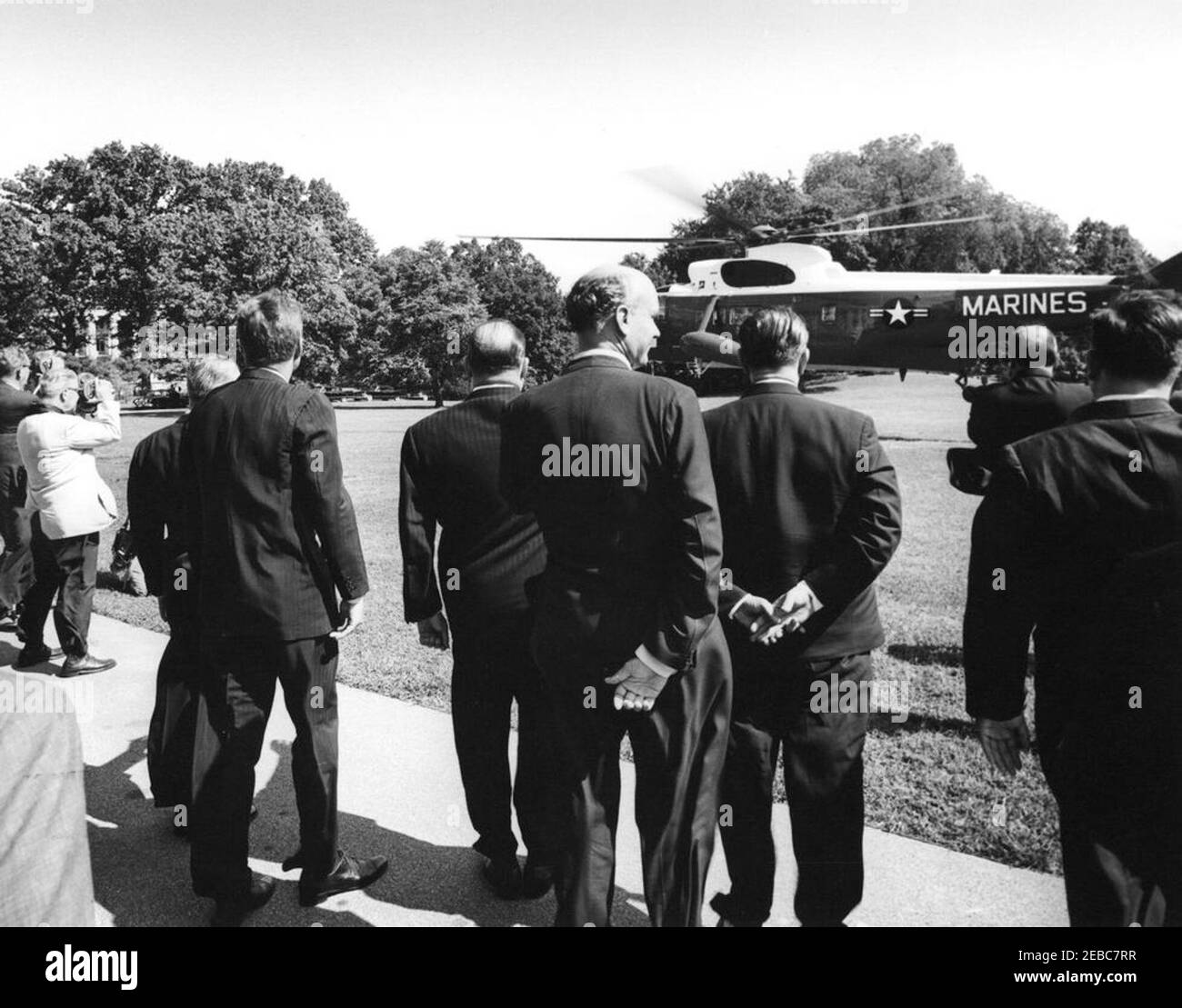 Ceremony marking Vice President Lyndon B. Johnsonu0027s (LBJ) departure on a good-will trip, 3:30PM. President John F. Kennedy (left, back to camera) watches as Vice President Lyndon B. Johnsonu2019s helicopter prepares to depart the South Lawn for his good-will trip to Lebanon, Iran, Turkey, Greece, Cyprus, and Italy. Ambassador of Nicaragua and Dean of the Diplomatic Corps, Dr. Guillermo Sevilla-Sacasa, stands right of President Kennedy; Ambassador of Italy, Sergio Fenoaltea (partially hidden), stands left of the President. Other unidentified officials, unidentified photographers, and repo Stock Photo