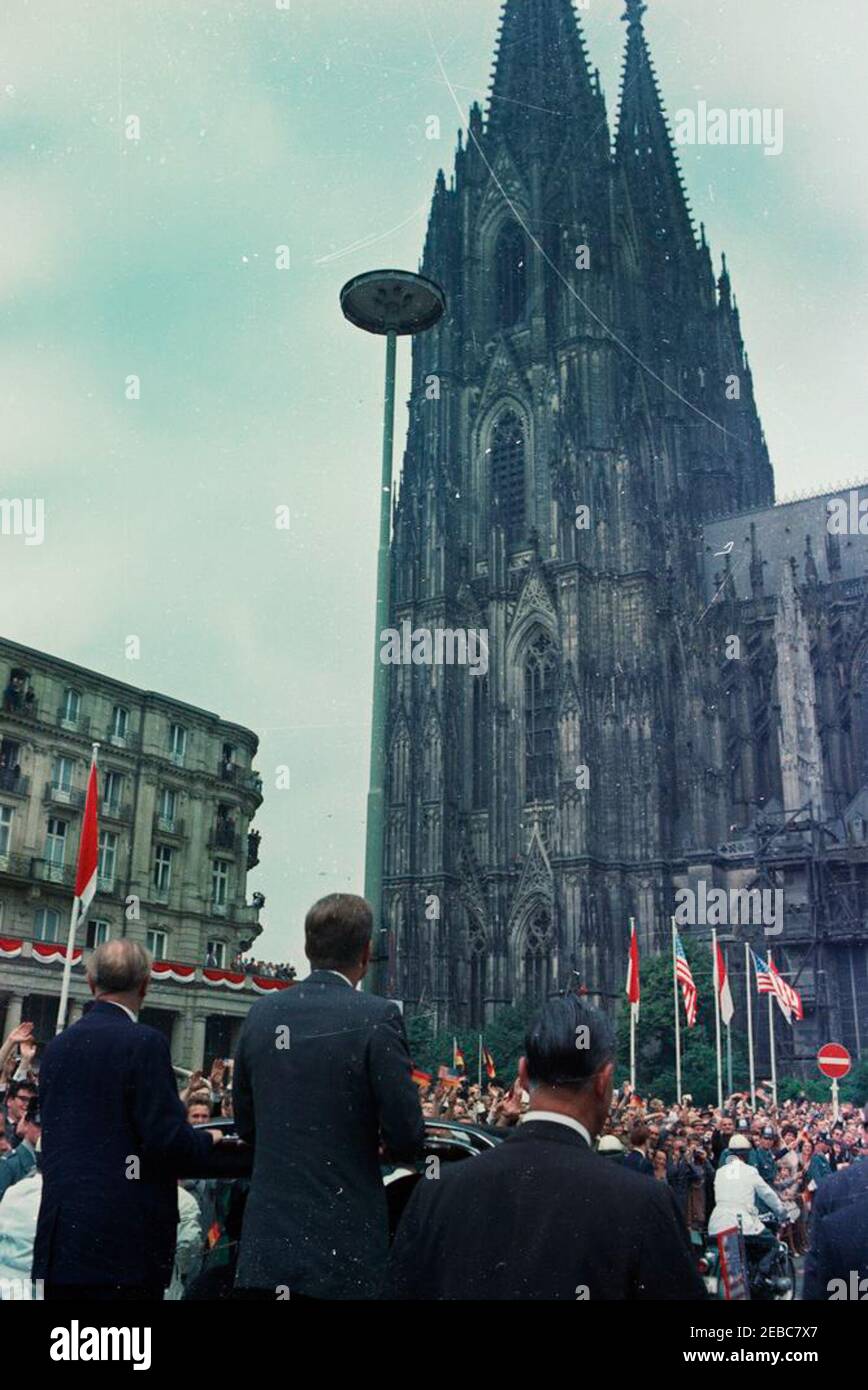 Trip to Europe: Germany, Cologne: Motorcade, Cathedral. President John F. Kennedy (center, back to camera) stands in an open convertible as his motorcade approaches the Cologne Cathedral; Chancellor of West Germany, Konrad Adenauer, stands left of President Kennedy. Cologne, West Germany (Federal Republic). Crowds line the street. Stock Photo