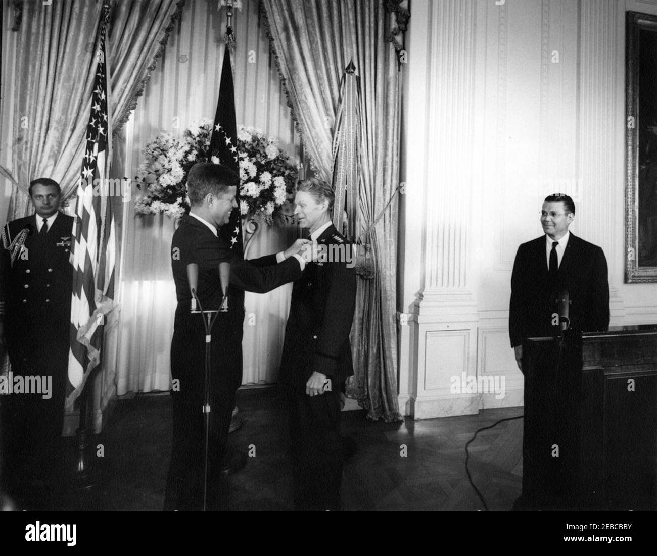 Presentation of the Distinguished Service Medal (DSM) to Gen. Lauris Norstad, 12:45PM. President John F. Kennedy presents the Distinguished Service Medal to retired Supreme Allied Commander of NATO, General Lauris Norstad; President Kennedy (center left) pins the medal to General Norstadu0027s lapel. Naval Aide to the President, Captain Tazewell T. Shepard, Jr., stands at left, in the background; Secretary of Defense, Robert S. McNamara (standing behind lectern), observes at right. East Room, White House, Washington, D.C. Stock Photo