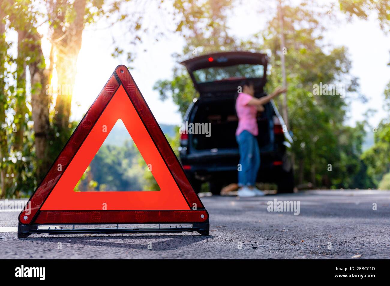Close up red emergency stop sign standing on road. Worried and angry woman walking near his broken car talking on phone with insurance agent. Close up Stock Photo