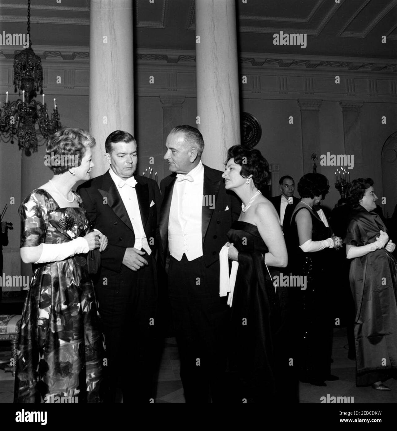 Dinner in honor of Vice President Lyndon B. Johnson (LBJ), Speaker of the House John W. McCormack, u0026 Chief Justice Earl Warren, 8:00PM. Vice President Lyndon B. Johnson (third from left) and Lady Bird Johnson visit with unidentified guests at a dinner in honor of Vice President Johnson, Speaker of the House of Representatives John W. McCormack, and Supreme Court Chief Justice Earl Warren. Standing in the background at right are (L-R): Chairman of the Atomic Energy Commission Glenn T. Seaborg; Beryl Hastie, wife of Judge William H. Hastie (facing away); Judge Hastie (mostly hidden); and Dr Stock Photo
