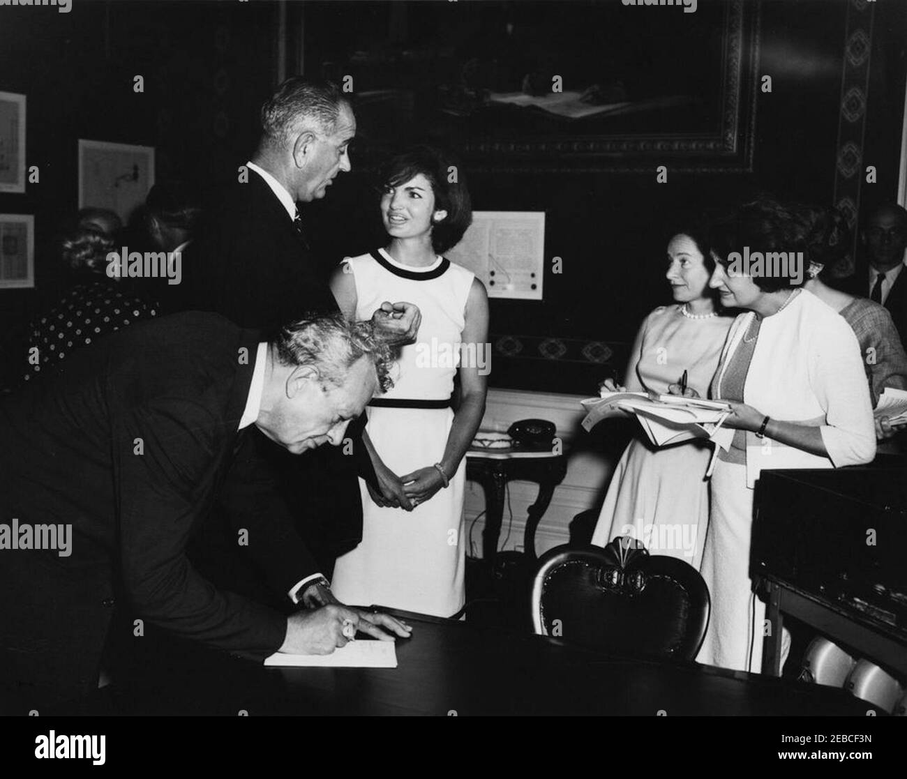 First Lady Jacqueline Kennedy (JBK) opens the refurbished Treaty Room. First Lady Jacqueline Kennedy speaks with Vice President Lyndon B. Johnson at the opening of the newly refurbished Treaty Room (formerly the Monroe Room). Senator Everett Dirksen (Illinois) leans over table at left; White House correspondent for United Press International (UPI), Helen Thomas, stands at right (wearing white jacket). White House Washington, D.C. Stock Photo