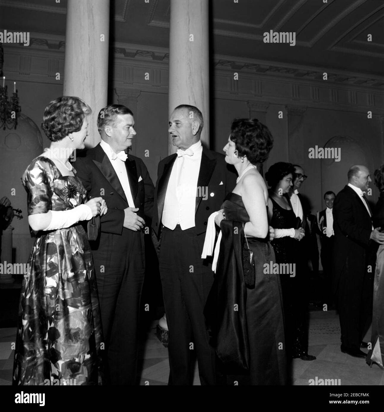 Dinner in honor of Vice President Lyndon B. Johnson (LBJ), Speaker of the House John W. McCormack, u0026 Chief Justice Earl Warren, 8:00PM. Vice President Lyndon B. Johnson (third from left) and Lady Bird Johnson visit with unidentified guests at a dinner in honor of Vice President Johnson, Speaker of the House of Representatives John W. McCormack, and Supreme Court Chief Justice Earl Warren. Standing in the background at right are (L-R): Beryl Hastie, wife of Judge William H. Hastie; Judge Hastie; Administrator of the Housing and Home Finance Agency Robert C. Weaver; and Dr. Ella Haith Weave Stock Photo