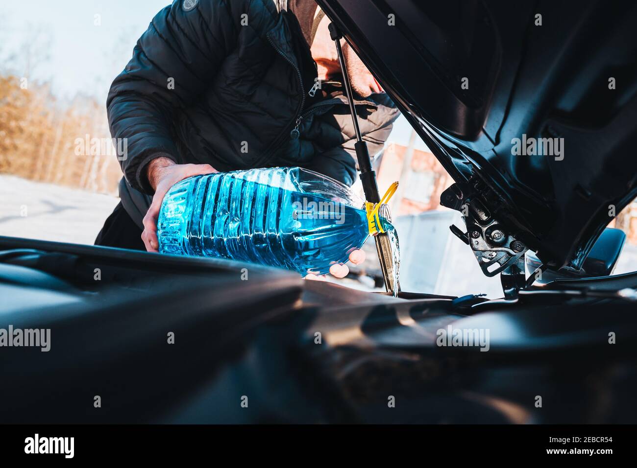 A man pours blue antifreeze liquid from a can into a car washer tank - winter maintenance Stock Photo