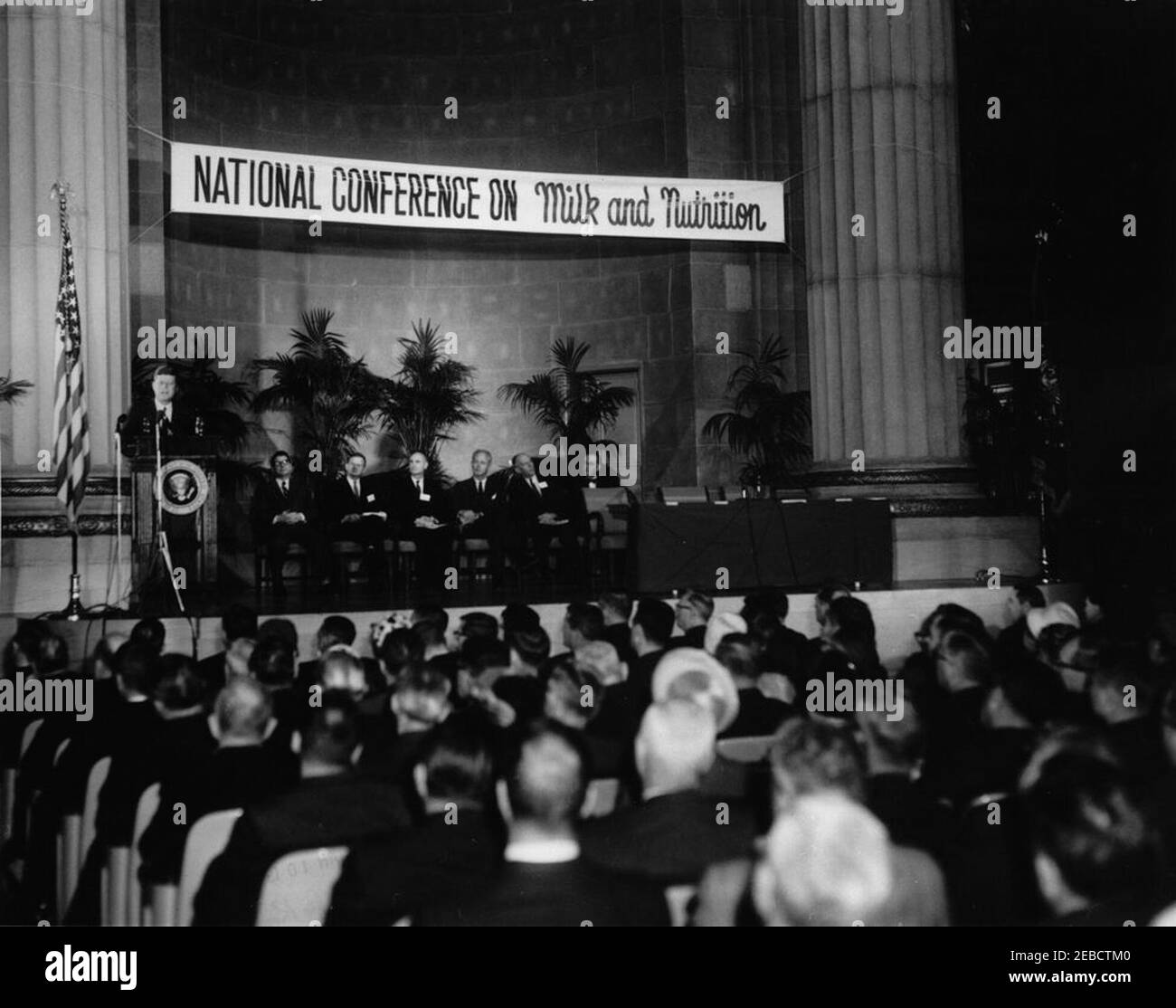 Address before the National Conference on Milk and Nutrition, 10:32AM. President John F. Kennedy speaks to an audience during the National Conference on Milk and Nutrition. Among those seated on stage are: Secretary of Agriculture Orville Freeman; Director of the Youth Physical Fitness Program Charles B. u201cBudu201d Wilkinson; Robert G. Lewis, Deputy Administrator for Price and Stabilization of the Agricultural Stabilization and Conservation Service; and Herb Jones of the Department of Agriculture. Departmental Auditorium, Washington, D.C. Stock Photo