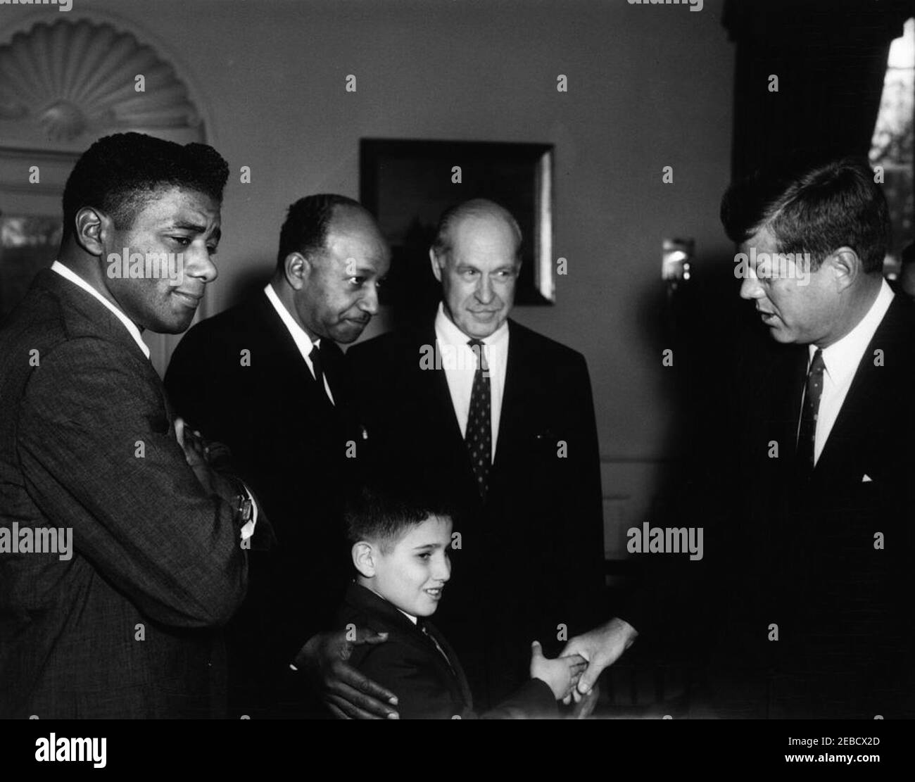 Visit of members of the Big Brothers Association, including Heavyweight Boxing Champion Floyd Patterson, 12:25PM. President John F. Kennedy greets representatives of the Big Brothers Association in connection with Big Brothers Week. The President shakes hands with ten-year-old Freddie Cicala, a u201clittle brotheru201d member of the Big Brothers organization. Looking on are (L-R): World heavyweight boxing champion Floyd Patterson; John Duncan, member of the District of Columbia Board of Commissioners; and journalist Drew Pearson. Oval Office, White House, Washington, D.C. Stock Photo