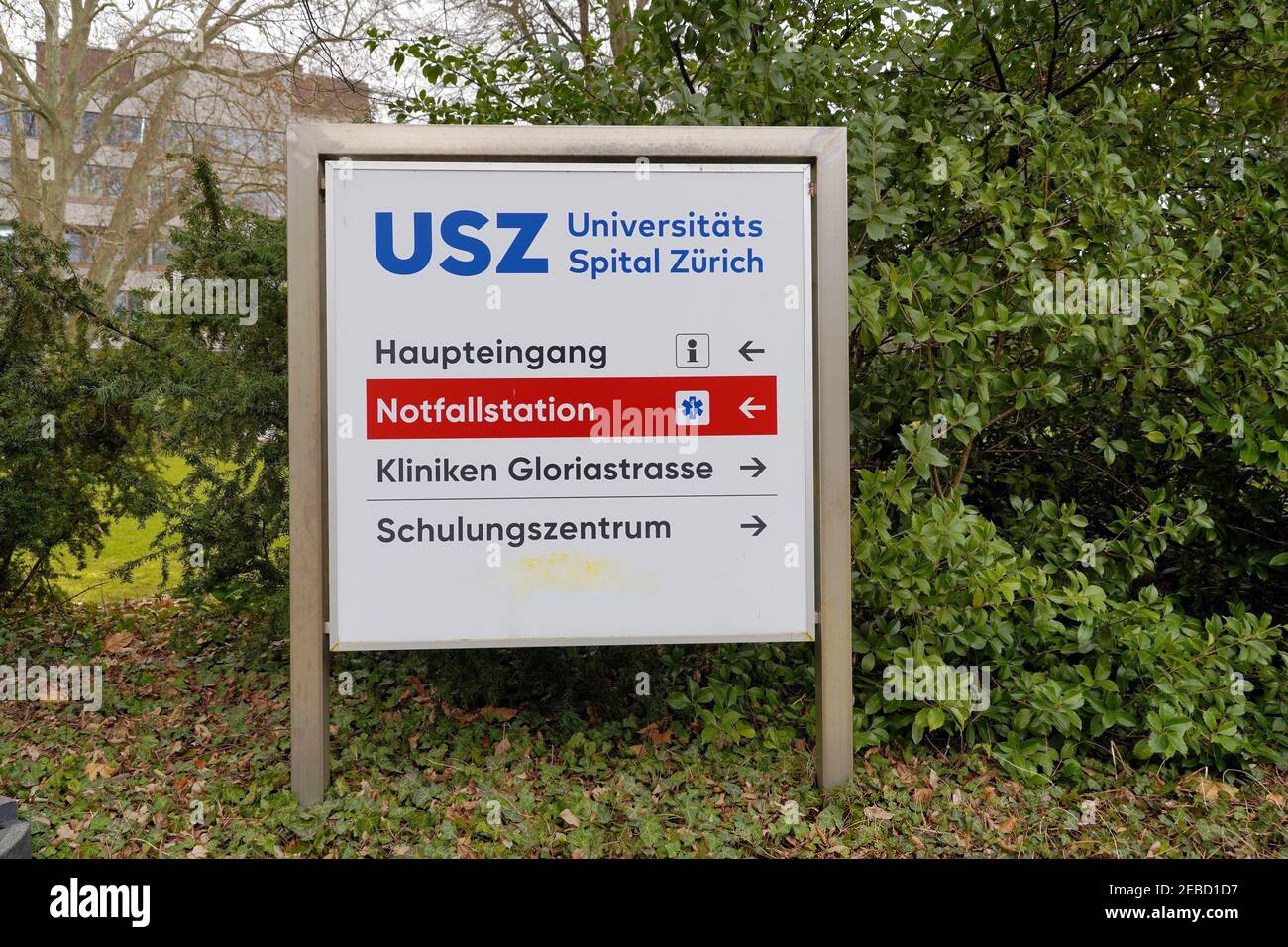 Signpost of Emergency room or E.R. direction at University Zurich Hospital with the building itself in the background. Directions are in German. Stock Photo