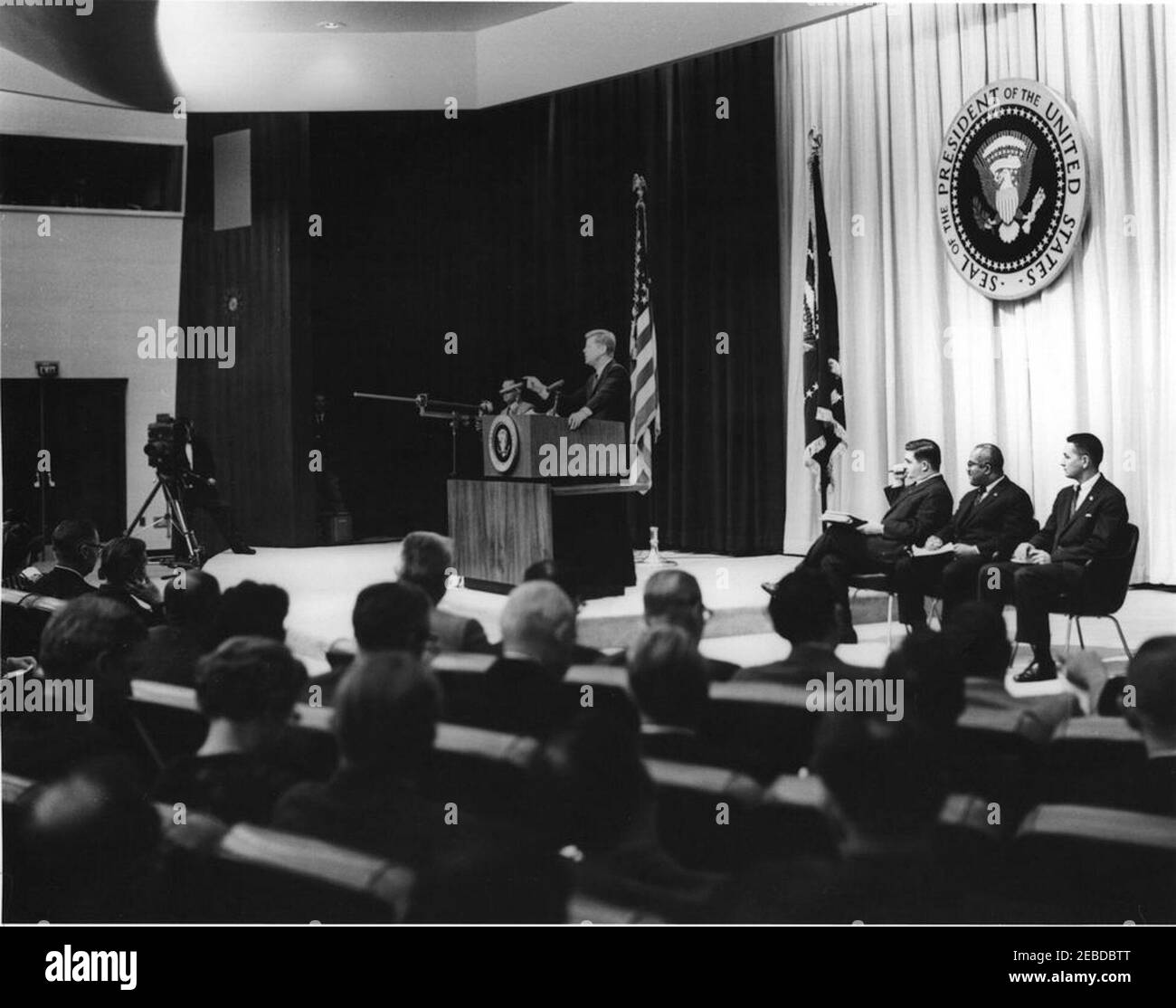 Press Conference, State Department Auditorium, 4:00PM. President John F. Kennedy (standing at lectern) speaks to reporters at a press conference. Sitting on stage (L-R): White House Press Secretary Pierre Salinger, Associate Press Secretary Andrew Hatcher, and Assistant White House Press Secretary Jay Gildner. State Department Auditorium, Washington, D.C. Stock Photo