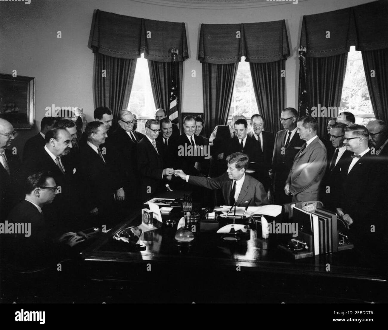 Bill signing - S. 2965 Public Law 87658, Accelerated Public Works Program, 9:30AM. President John F. Kennedy (seated at desk) hands a pen to Senator Dennis Chu00e1vez (New Mexico) after signing S. 2965, the Public Works Acceleration Act. Left to right: unidentified stenographer (seated); Senator Oren E. Long (Hawaii); Secretary of the Department of Health, Education, and Welfare (HEW), Anthony J. Celebrezze; Representative Walter H. Moeller and Senator Stephen M. Young, both of Ohio; Senator Edmund S. Muskie (Maine); Senator Pat McNamara (Michigan); Senator Chu00e1vez (receiving a pen from P Stock Photo