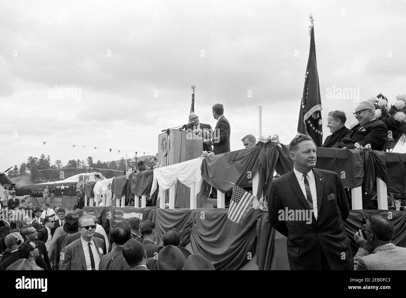 Trip to Oklahoma: Ribbon cutting ceremony at Ouachita National Park Road, Big Cedar, Oklahoma. President John F. Kennedy attends ribbon cutting ceremony at Ouachita National Forest Road. Oklahoma Senator Robert Kerr (left) and President Kennedy (facing away from camera) at lectern. Big Cedar, Oklahoma. Stock Photo