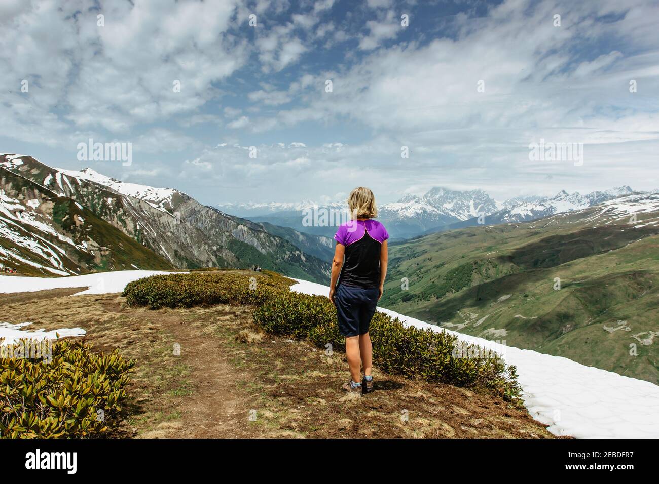 Girl standin on the top of a mountain,Georgia, snowy peaks in background.Backpacker enjoying view of mountain panorama.Wanderlust travel scene.Sporty Stock Photo