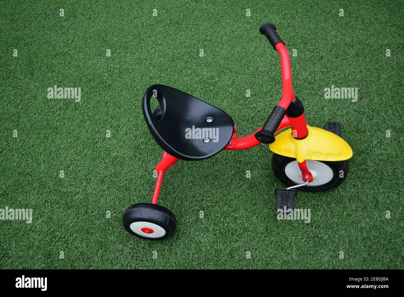 Red tricycle with a yellow mudguard on artificial grassready to ride Stock Photo