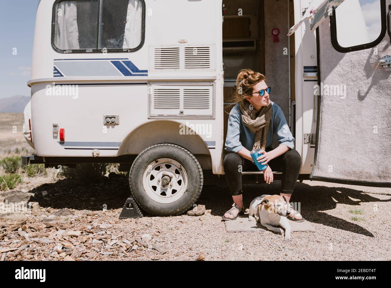 A stylish young woman and her dog sit outside their car trailer Stock Photo