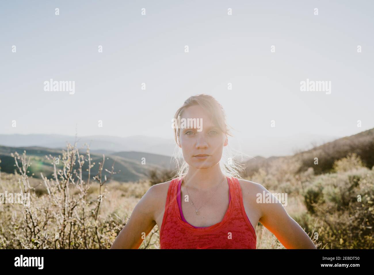 Athletic blonde woman stares back at you with sun and mountains behind Stock Photo