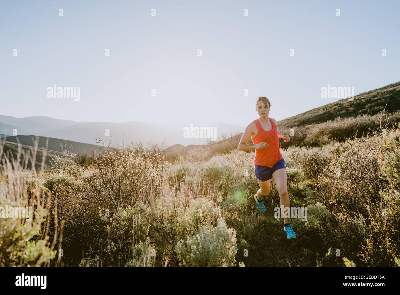 Athletic blonde woman trail runs in the mountains at golden hour Stock Photo