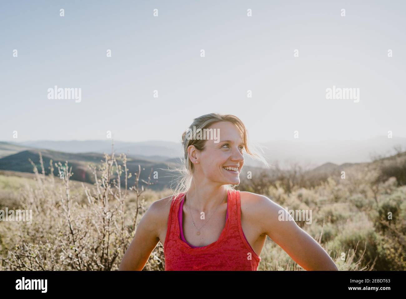 Athletic blonde woman laughs with sun and mountains behind her Stock Photo
