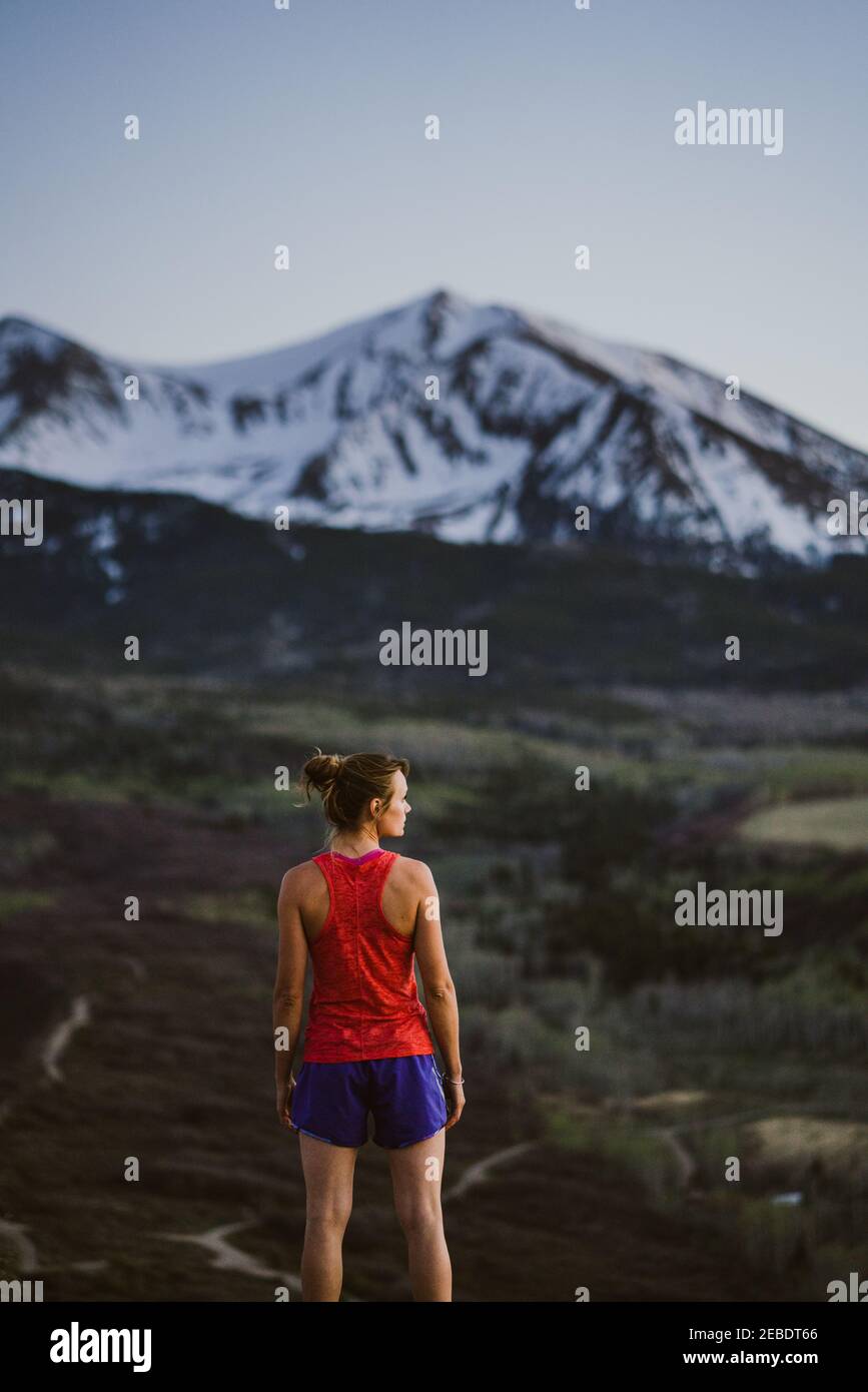 Young woman looks out at the mountains while trail running at dusk Stock Photo