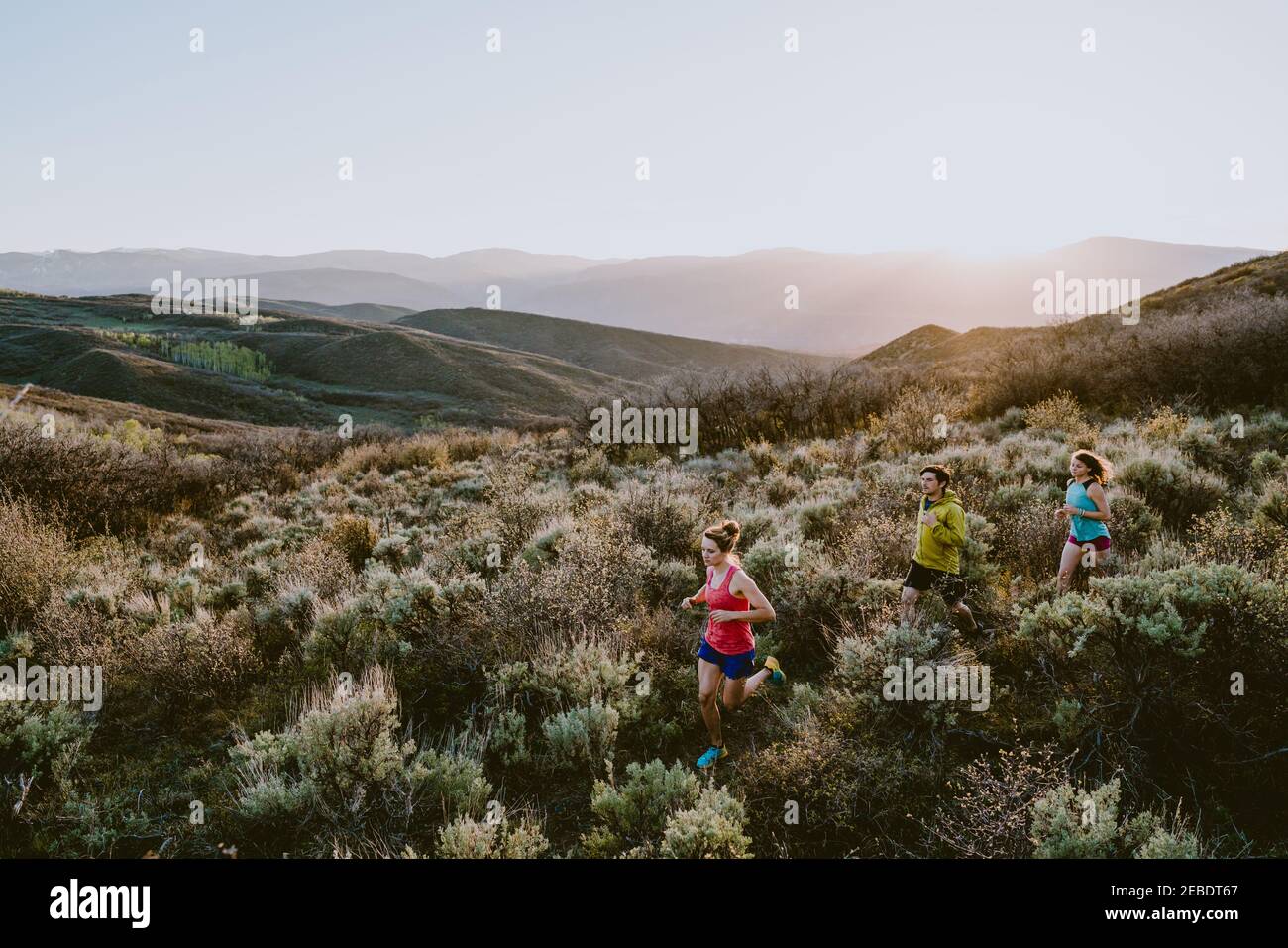 Three friends trail running in the mountains at golden hour Stock Photo