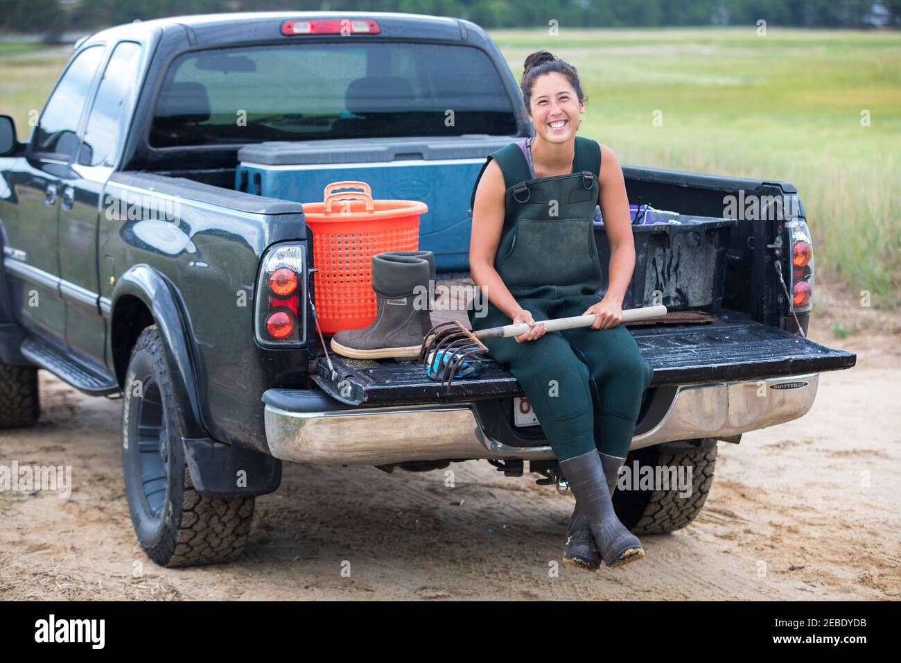 Asian woman in waders sits on truck before harvesting shellfish Stock Photo