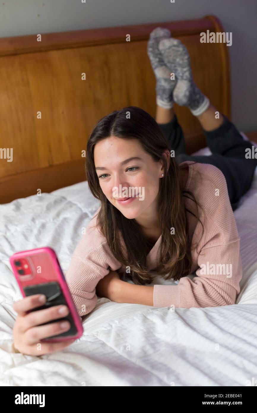 college-aged caucasian woman lying on bed taking selfie Stock Photo