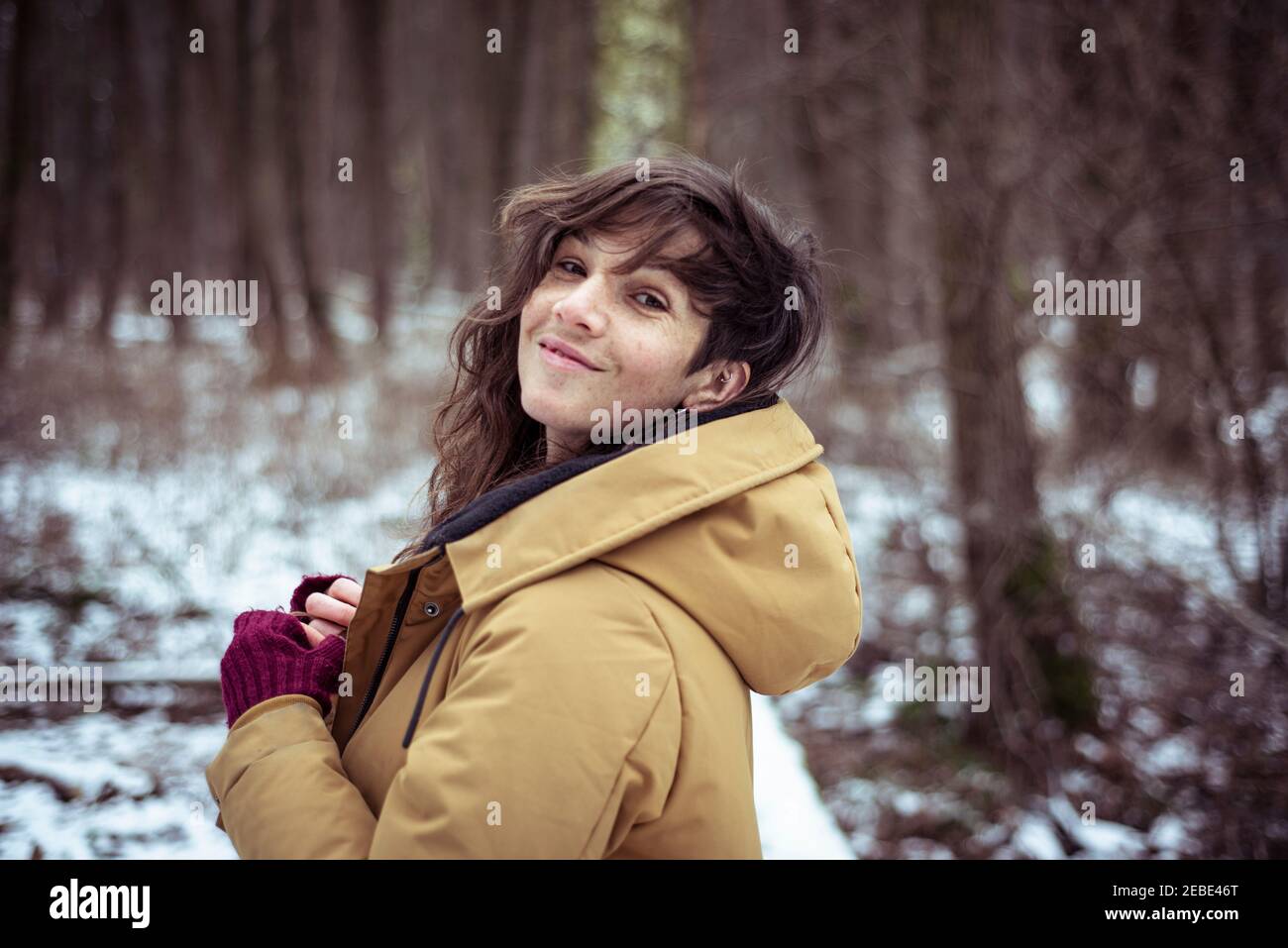 cheerful woman smiles cheekily over shoulder in snowy winter forrest Stock Photo