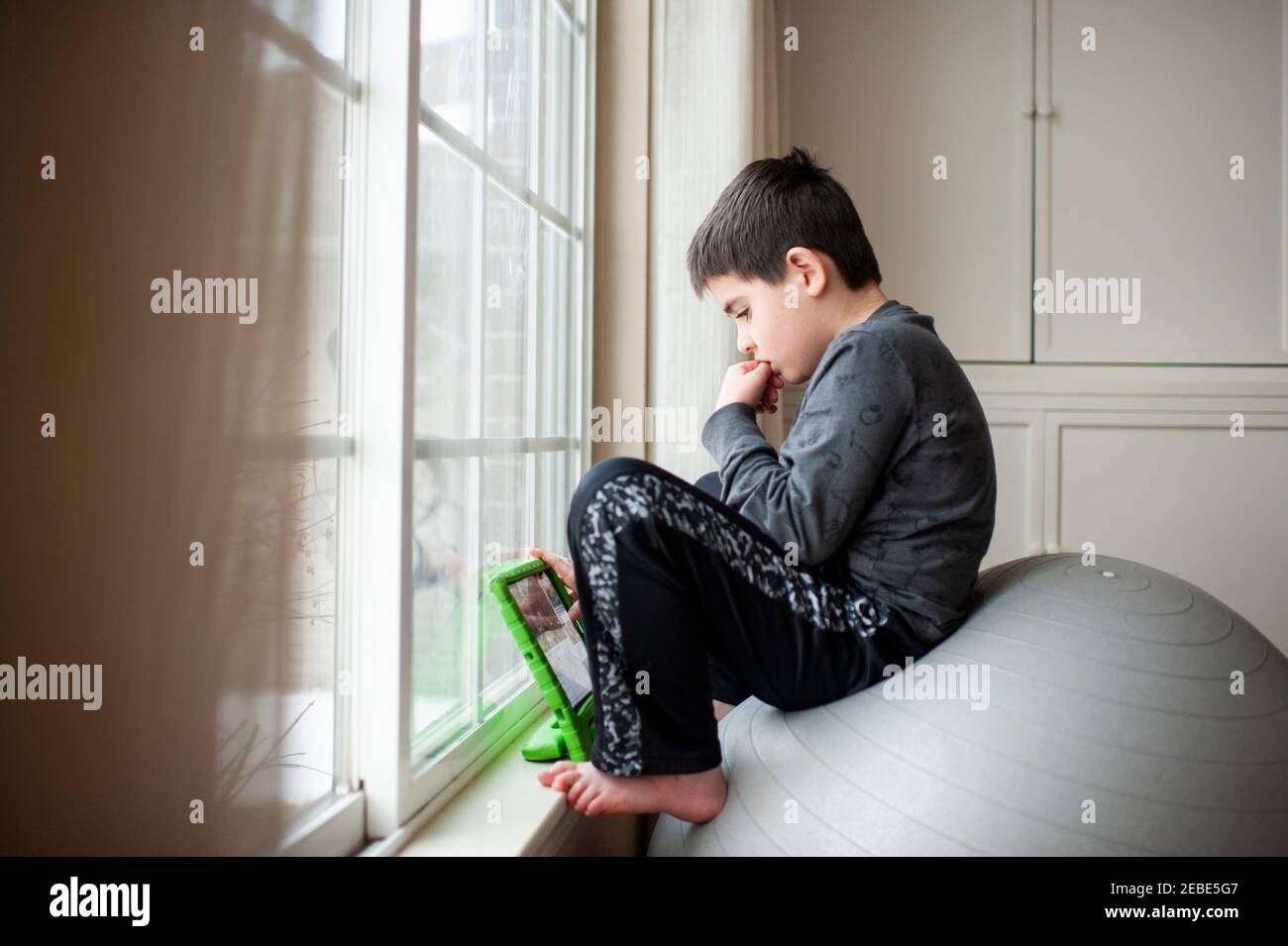 Boy 9-10 years old sits on exercise ball playing with his tablet Stock Photo