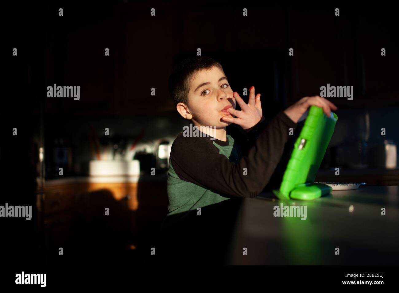 Boy 9-10 years old licks fingers while holding tablet in pretty light Stock Photo