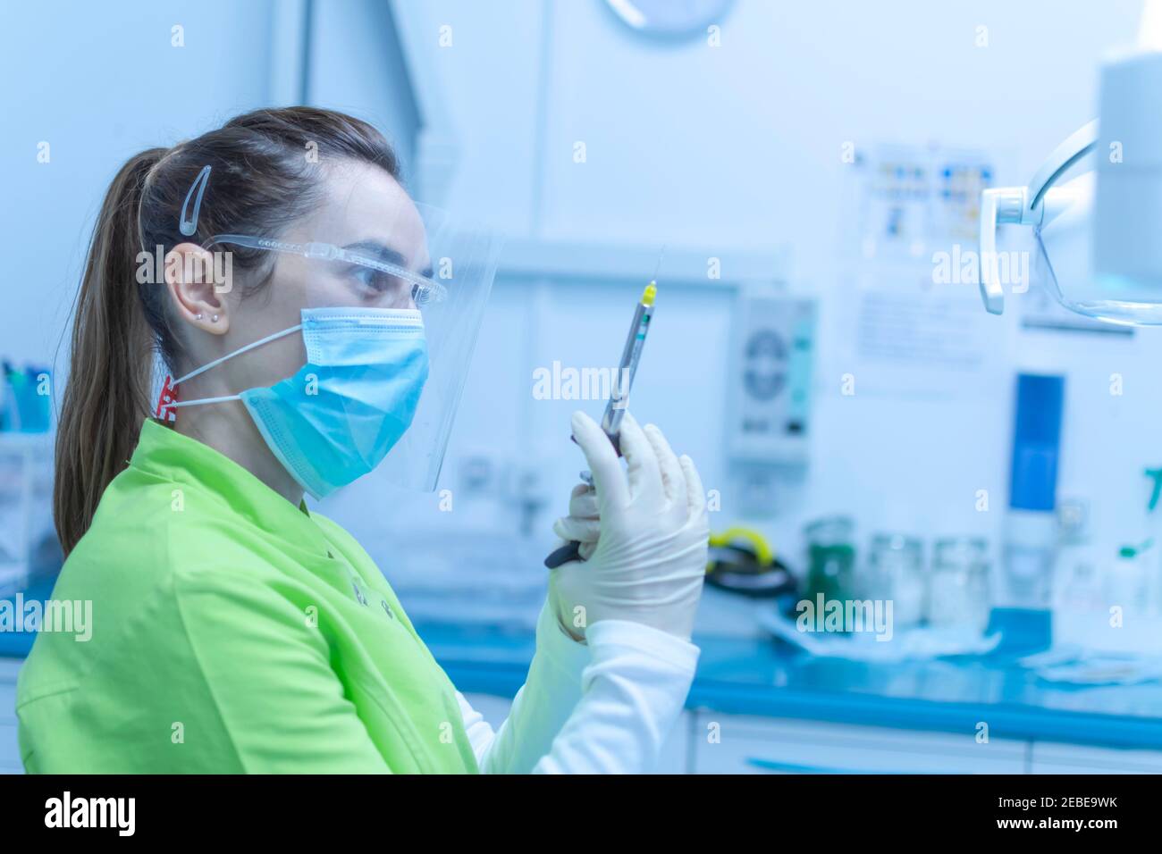 Female dentist preparing the anesthesia syringe wearing a mask hires