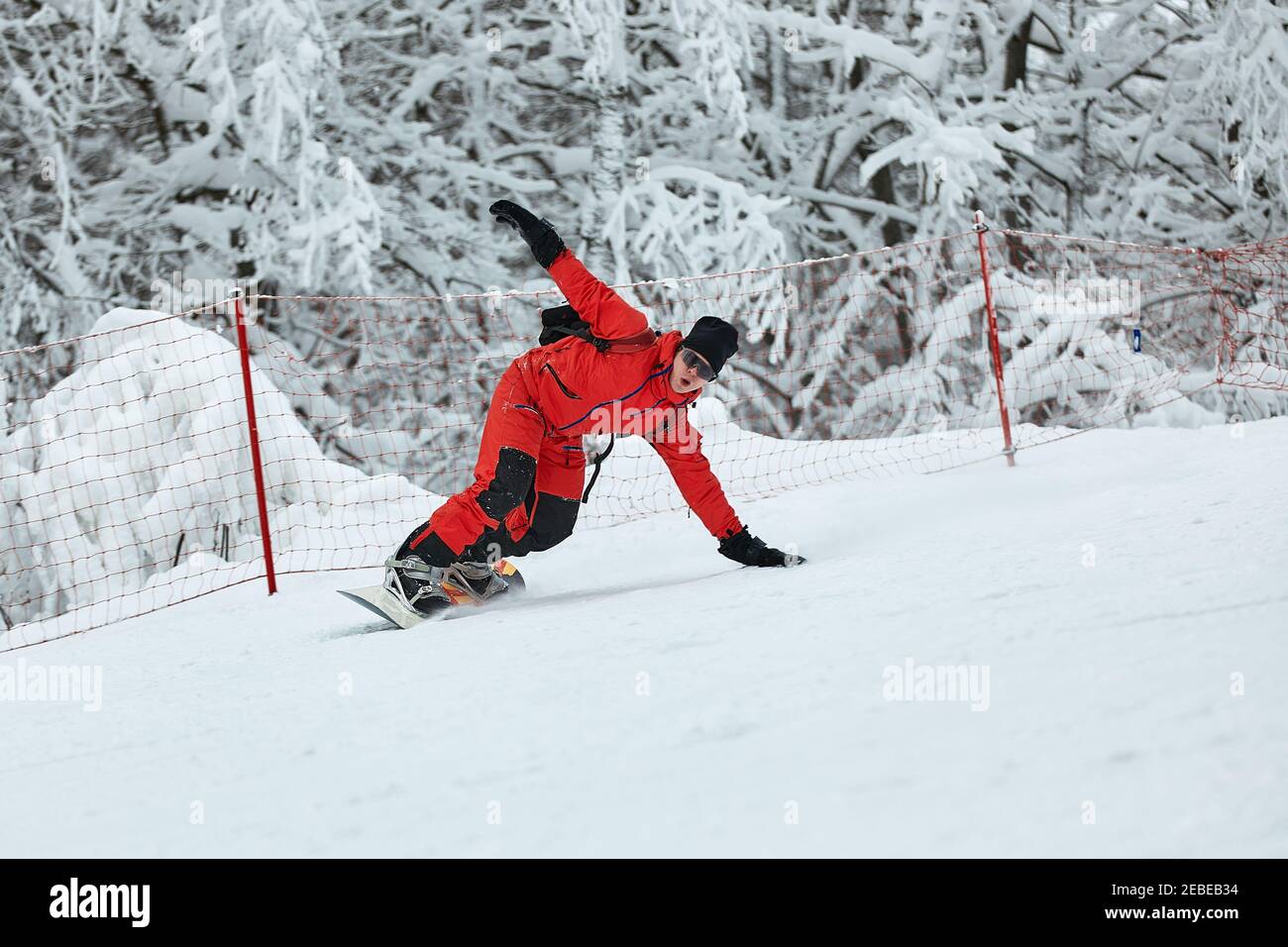 Male snowboarder in a red suit rides on the snowy hill with snowboard, Skiing and snowboarding concept. Stock Photo