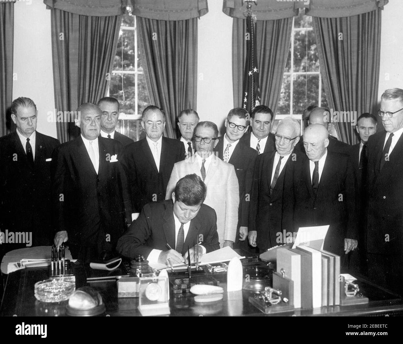 Bill signing, S. 1643 Public Law 87-128, Agricultural Act of 1961, 9:45 AM. President John F. Kennedy signs S. 1643, the Agricultural Act of 1961. The bill was legislated to improve farm income, expand the market for agricultural products, and reduce stocks of grains and wheat. Standing behind President Kennedy are (L-R): Senator Olin Johnston of South Carolina; Representative Harold D. Cooley of North Carolina; Vice President Lyndon B. Johnson; Senator Hubert Humphrey of Minnesota; Representative W.R. Poage of Texas; Senator Allen Ellender of Louisiana (white suit); Secretary of Agriculture O Stock Photo