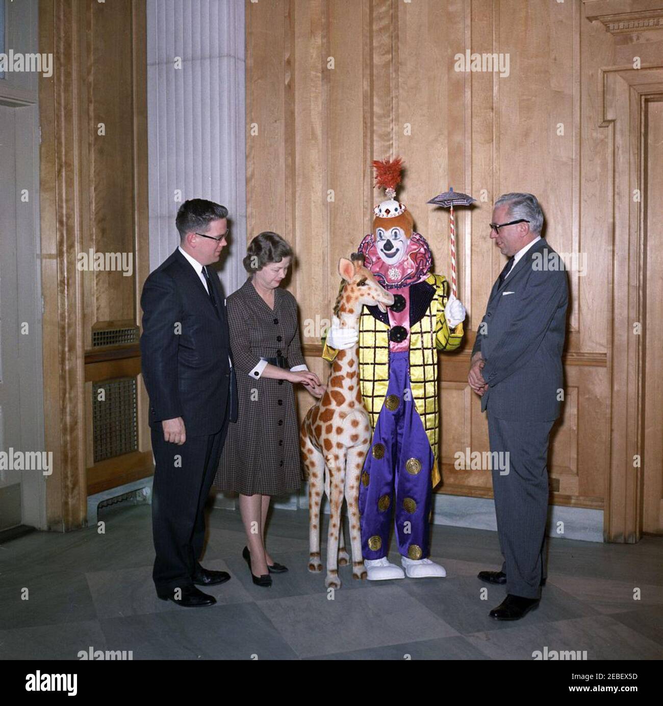 Ringling Bros. and Barnum u0026 Bailey Circus clown Jackie Le Claire presents a gift for Caroline Kennedy (CBK), with David Polland and Hortense Burton (John J. McNally). Ringling Bros. and Barnum u0026 Bailey Circus clown, Jackie LeClaire, presents a toy stuffed giraffe as a gift for Caroline Kennedy. L-R: Presidential Assistant, John J. McNally; Chief of the Correspondence Pool in the Social Entertainments Office, Hortense Burton; Mr. LeClaire; David Polland. East Wing Lobby, White House, Washington, D.C. Stock Photo
