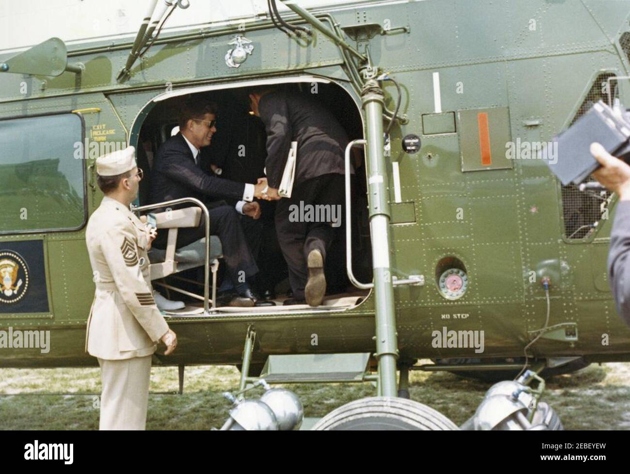 Commencement Address at the US Naval Academy, Annapolis, Maryland, 11:04AM. President John F. Kennedy (wearing sunglasses) sits inside a helicopter on the South Lawn of the White House en route to the commencement ceremony at the United States Naval Academy in Annapolis, Maryland. Stock Photo