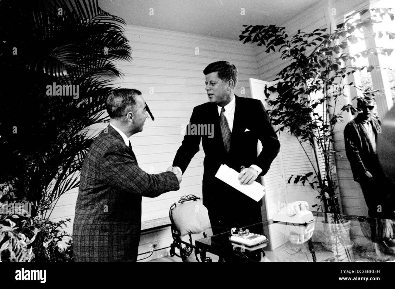 Opening ceremony for the Seattle Worldu0027s Fair from Palm Beach. President John F. Kennedy shakes hands with Robert Bright, of the American Telephone and Telegraph Company (ATu0026T), during the opening ceremony for the 1962 Seattle Worldu0027s Fair (also known as the Century 21 Exposition) from the residence of C. Michael Paul in Palm Beach, Florida. White House Secret Service agent, Clint Hill (wearing sunglasses), stands in background at right. President Kennedy delivered remarks by telephone and pressed a gold telegraph key (on patio table at bottom right) to open the fair via satelli Stock Photo