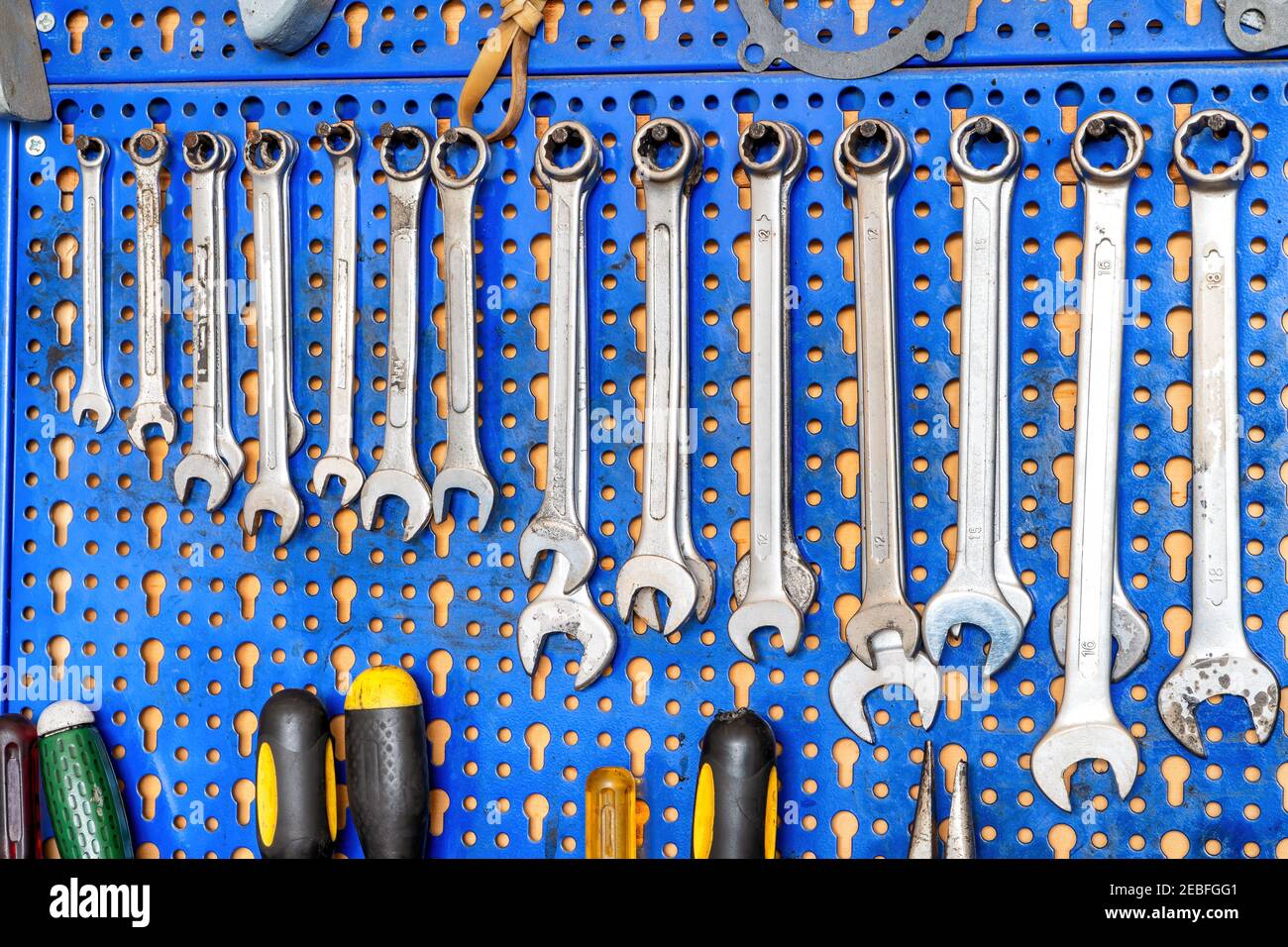 A range of used mechanic tools, from combination wrenches to screwdrivers. All hanging on blue panels. Perfect shot for arts and crafts. Stock Photo