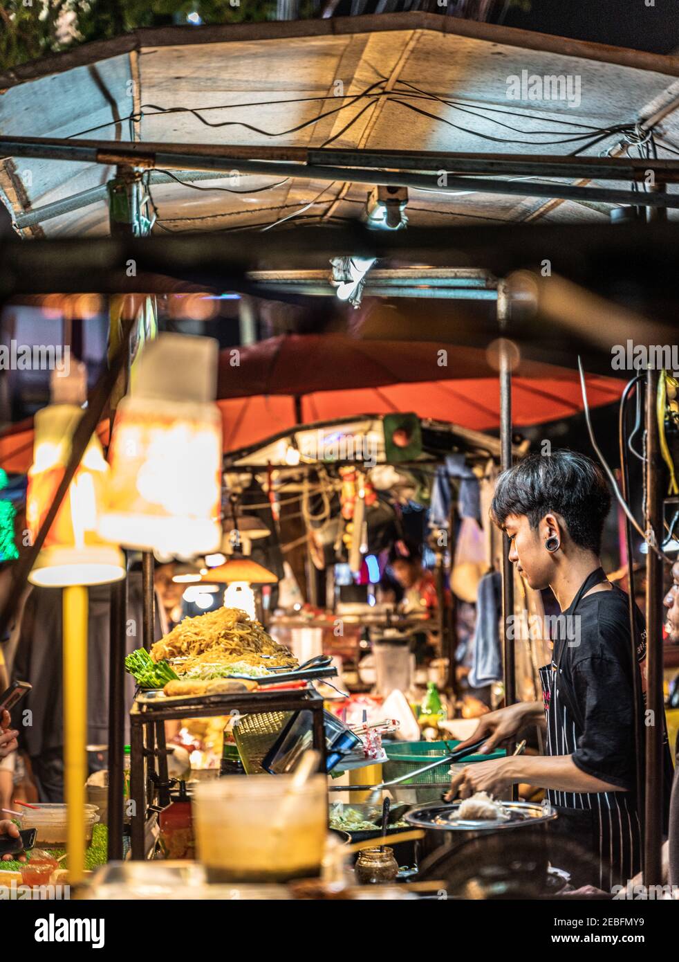 A cook prepares noodle dishes in a food Stall at Patong Night Market in Bangkok, Thailand. Stock Photo